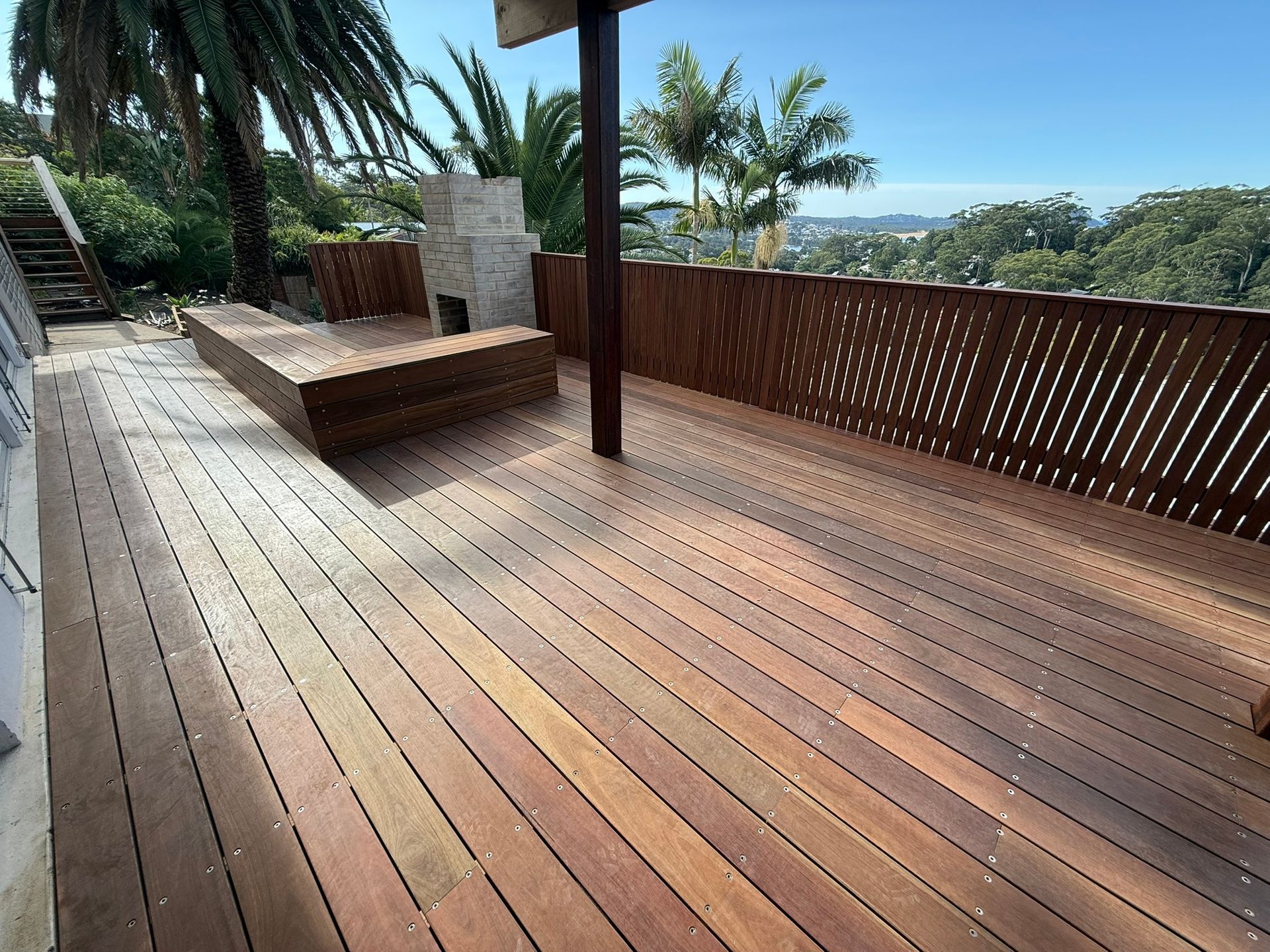 Wooden deck with built-in seating and palm trees overlooking a coastal view — Divine Landscape Creations in Berkeley Vale, NSW