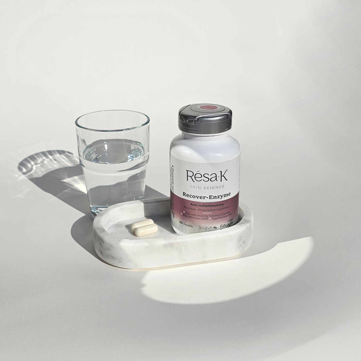 A bottle of pills and a glass of water on a marble tray.