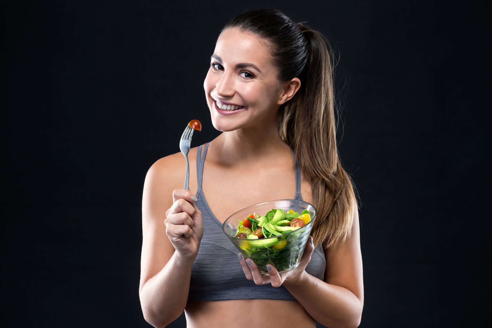 A woman is eating a salad with a fork and smiling.