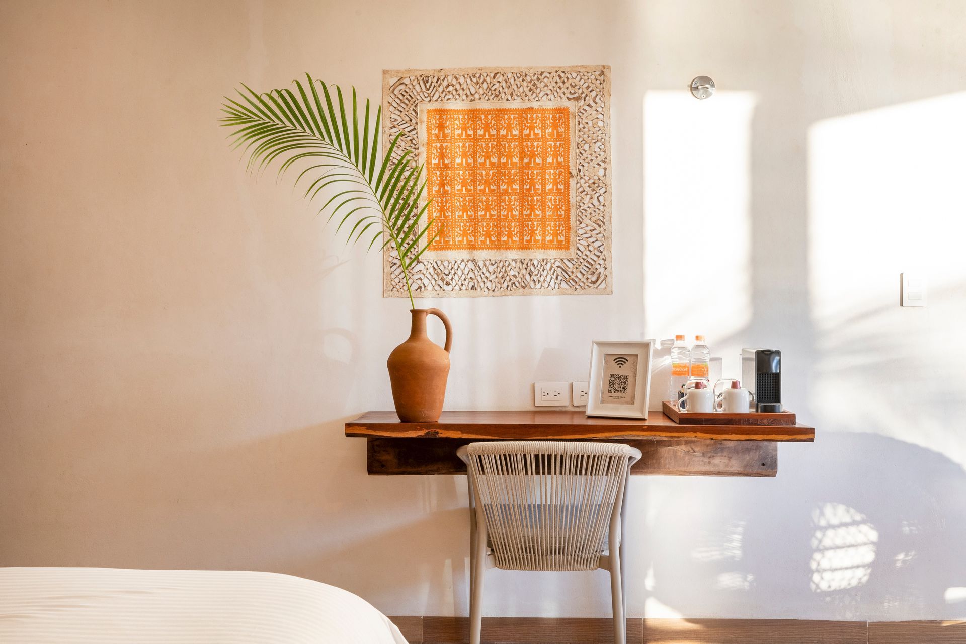 A wooden desk with decorations, a chair, and artwork against a white wall.