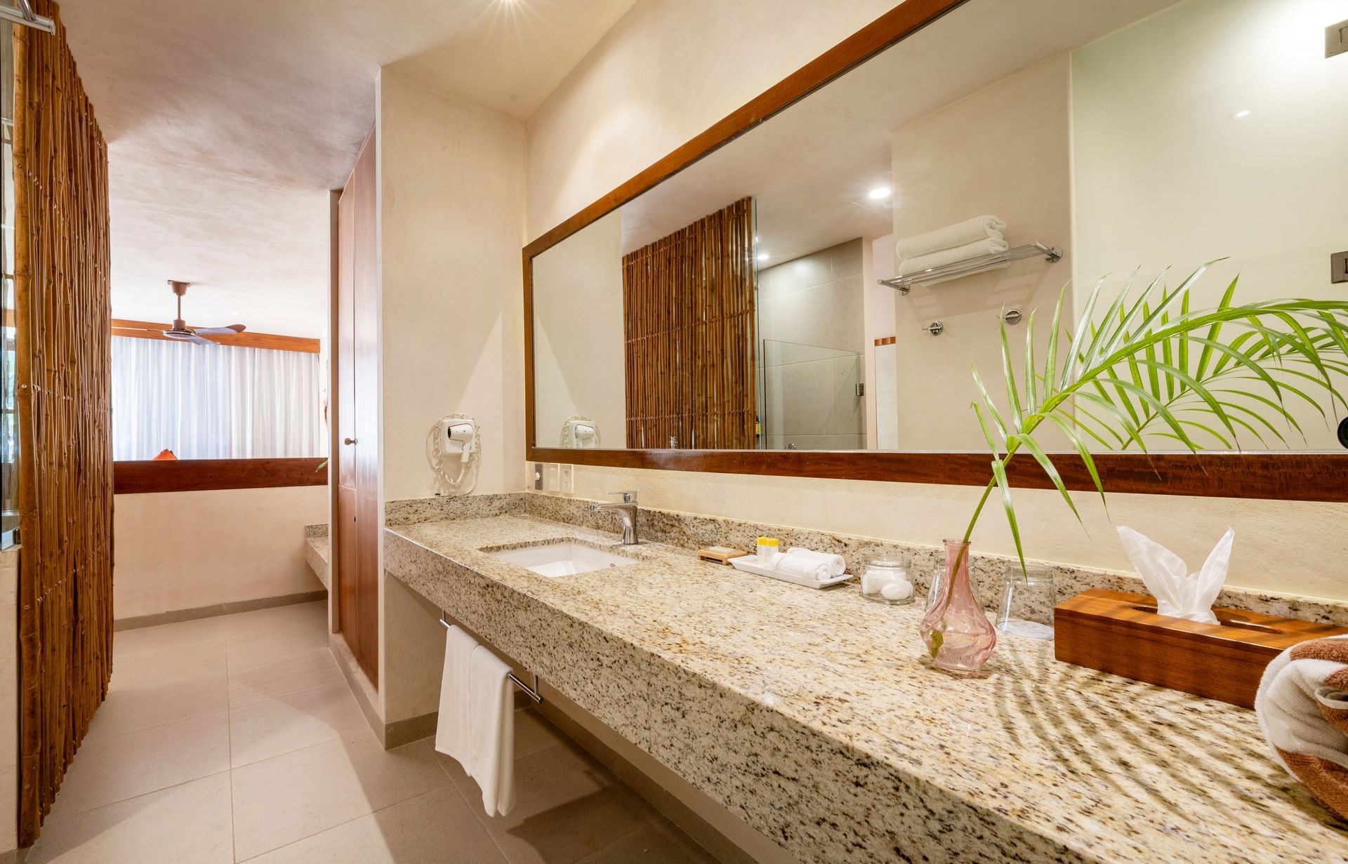 Bathroom with long granite countertop, large mirror, and open doorway to bedroom.