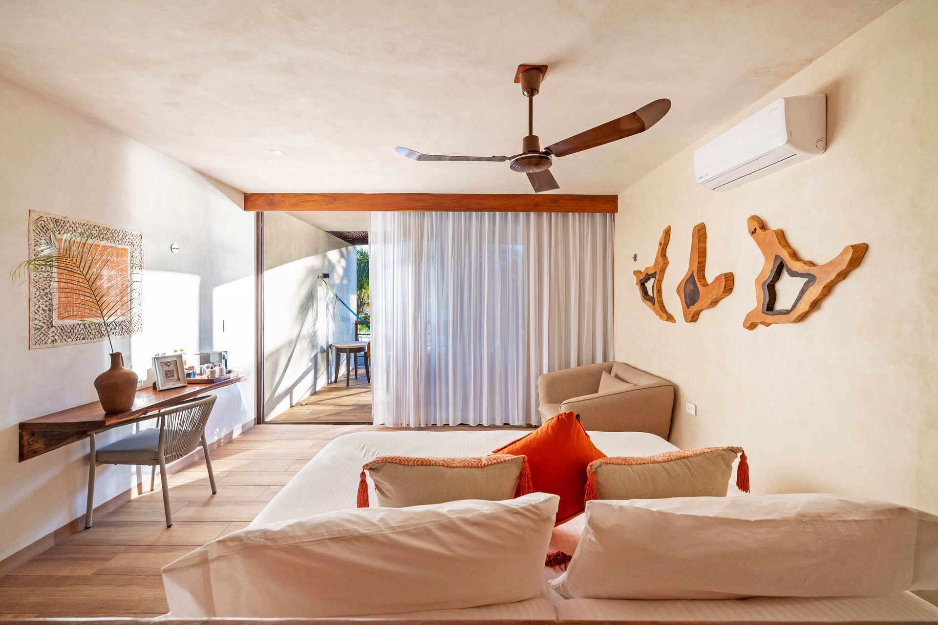 Bedroom with a bed, desk, balcony, and wooden wall decorations. Beige walls, white curtains.
