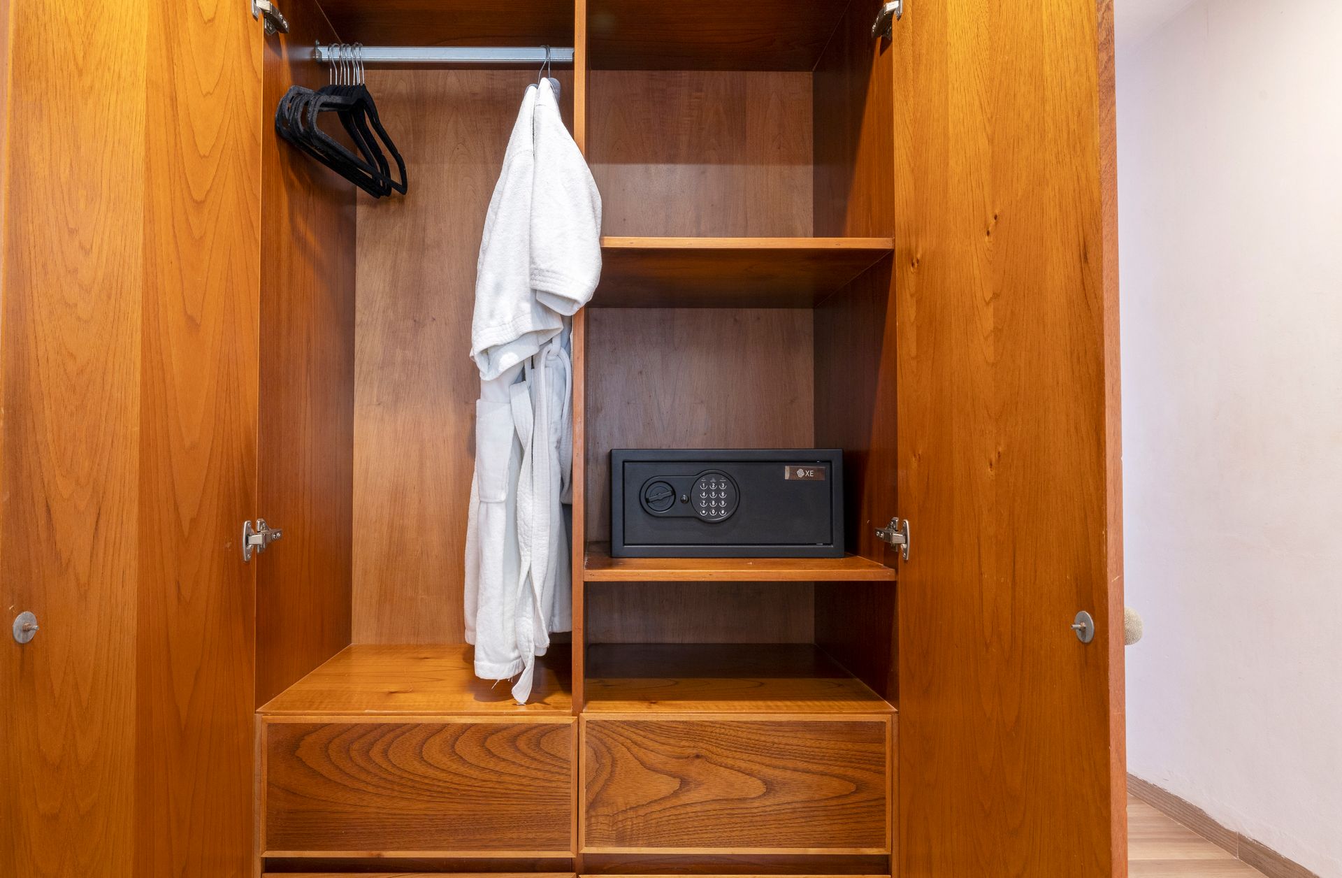 Wooden closet with a safe, clothes hanging, and drawers.