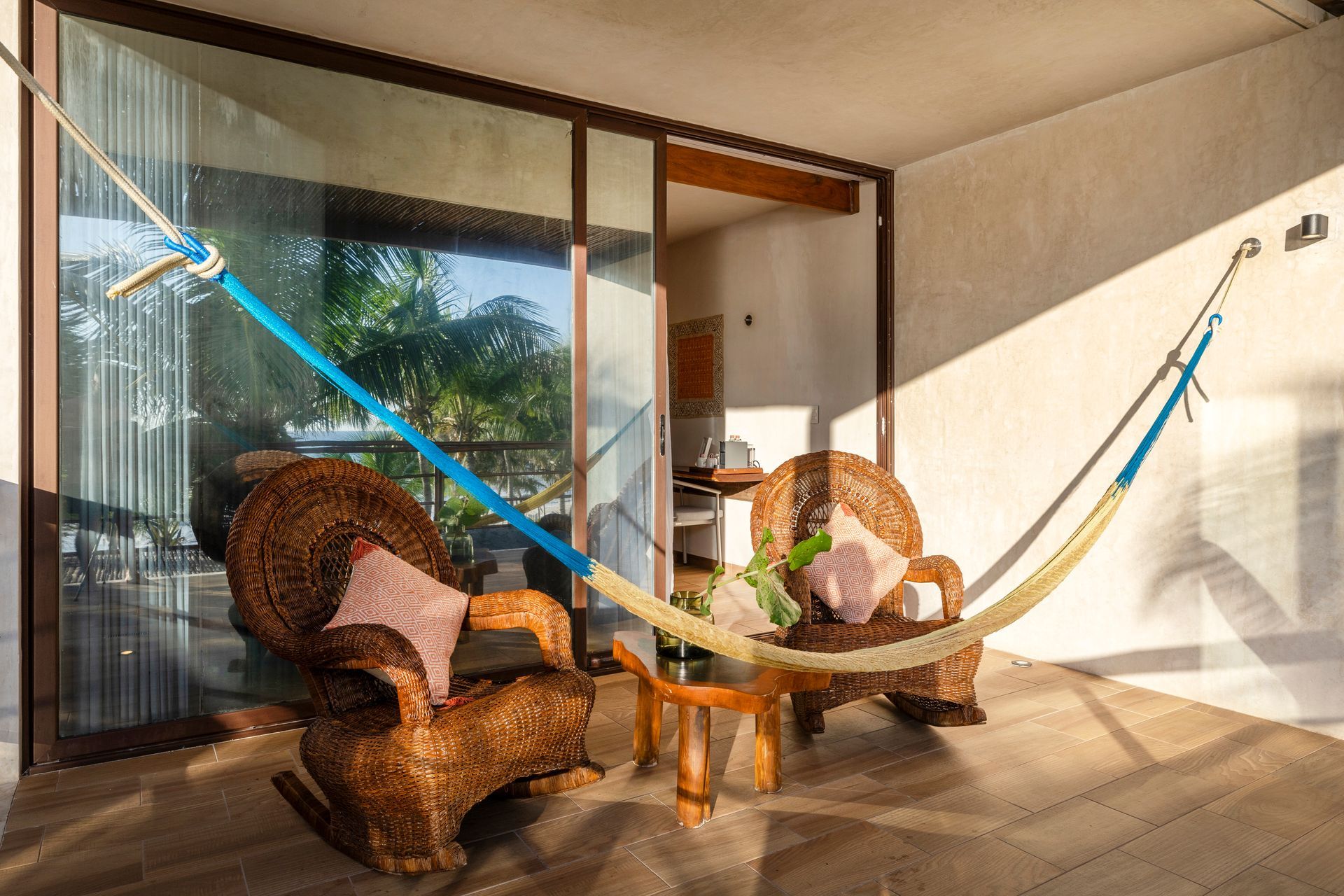 Balcony with hammock, wicker chairs, small table, and open sliding glass doors.