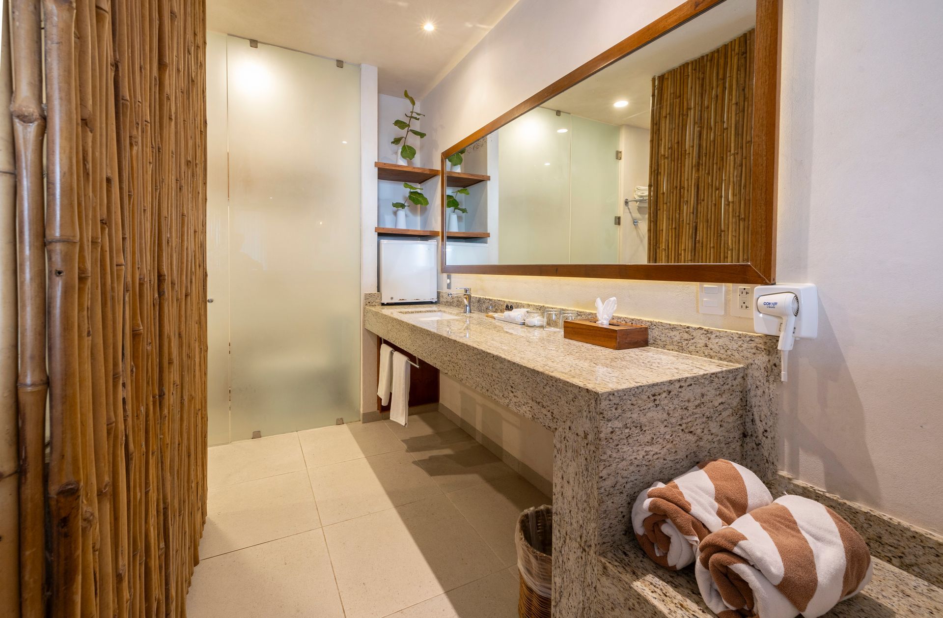 Bathroom with bamboo wall, stone countertop, large mirror, and towels.