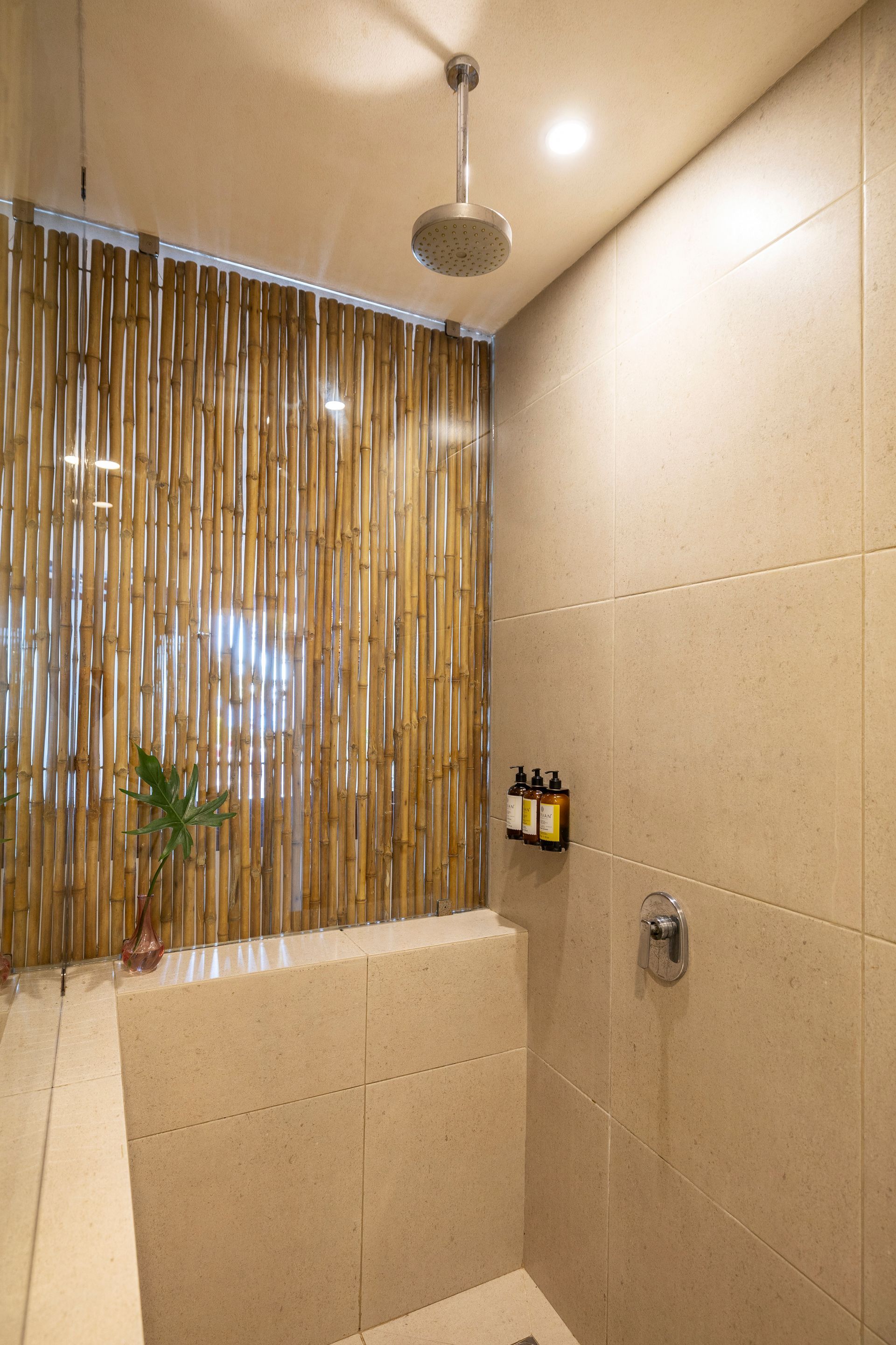 Shower stall with bamboo screen, overhead rain shower head, neutral tile walls, and a shelf with toiletries.