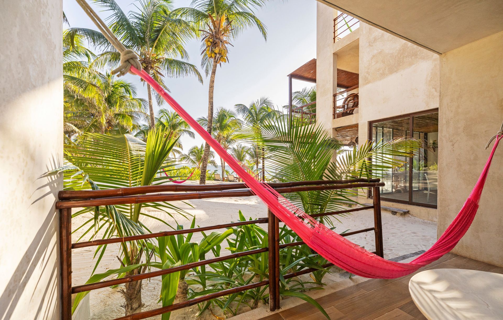 Pink hammock on a balcony with white gravel floor, lush green foliage, and a sunny view.