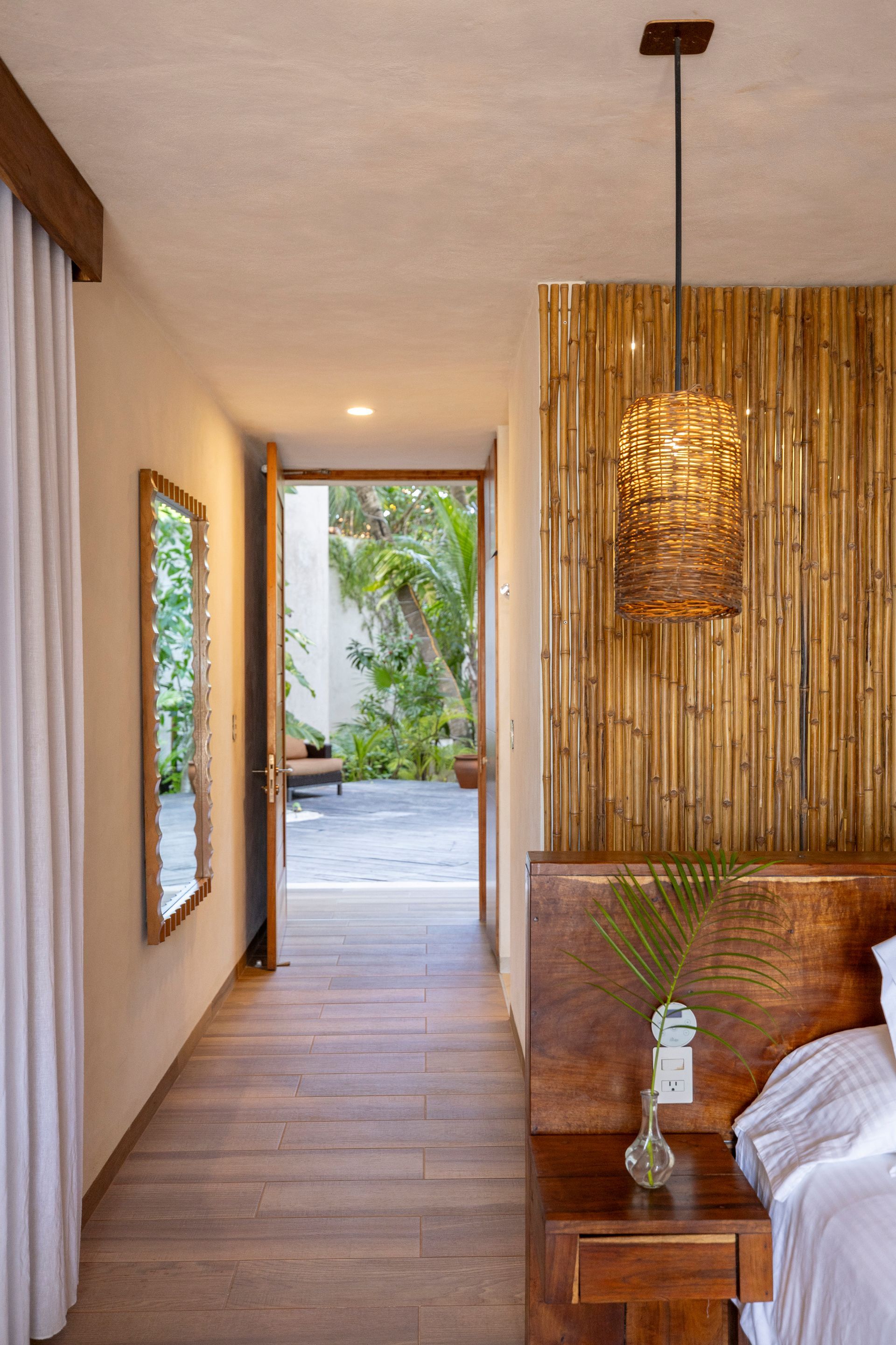 Bedroom hallway with wood flooring, open doorway to a courtyard, bamboo accent wall, and hanging pendant light.