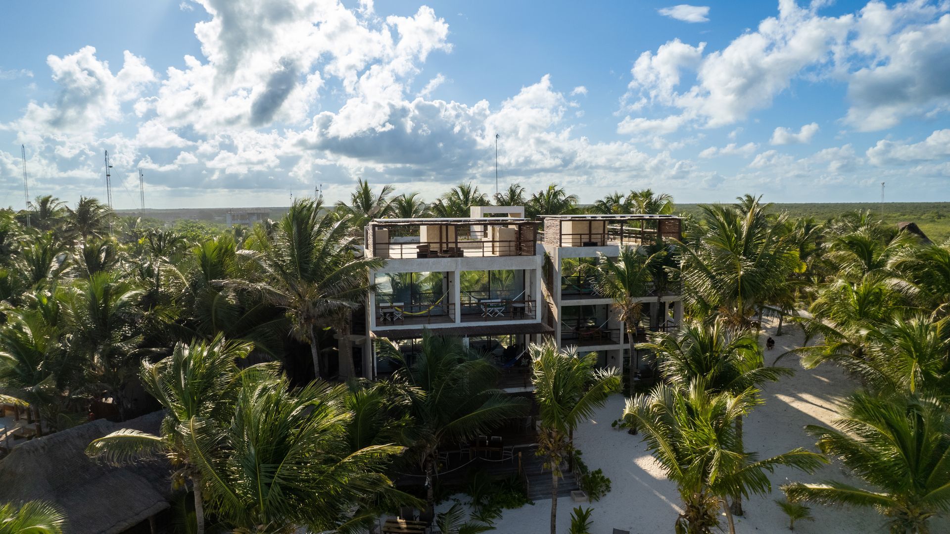 Multi-story structure amid palm trees, sunny day, blue sky with clouds.