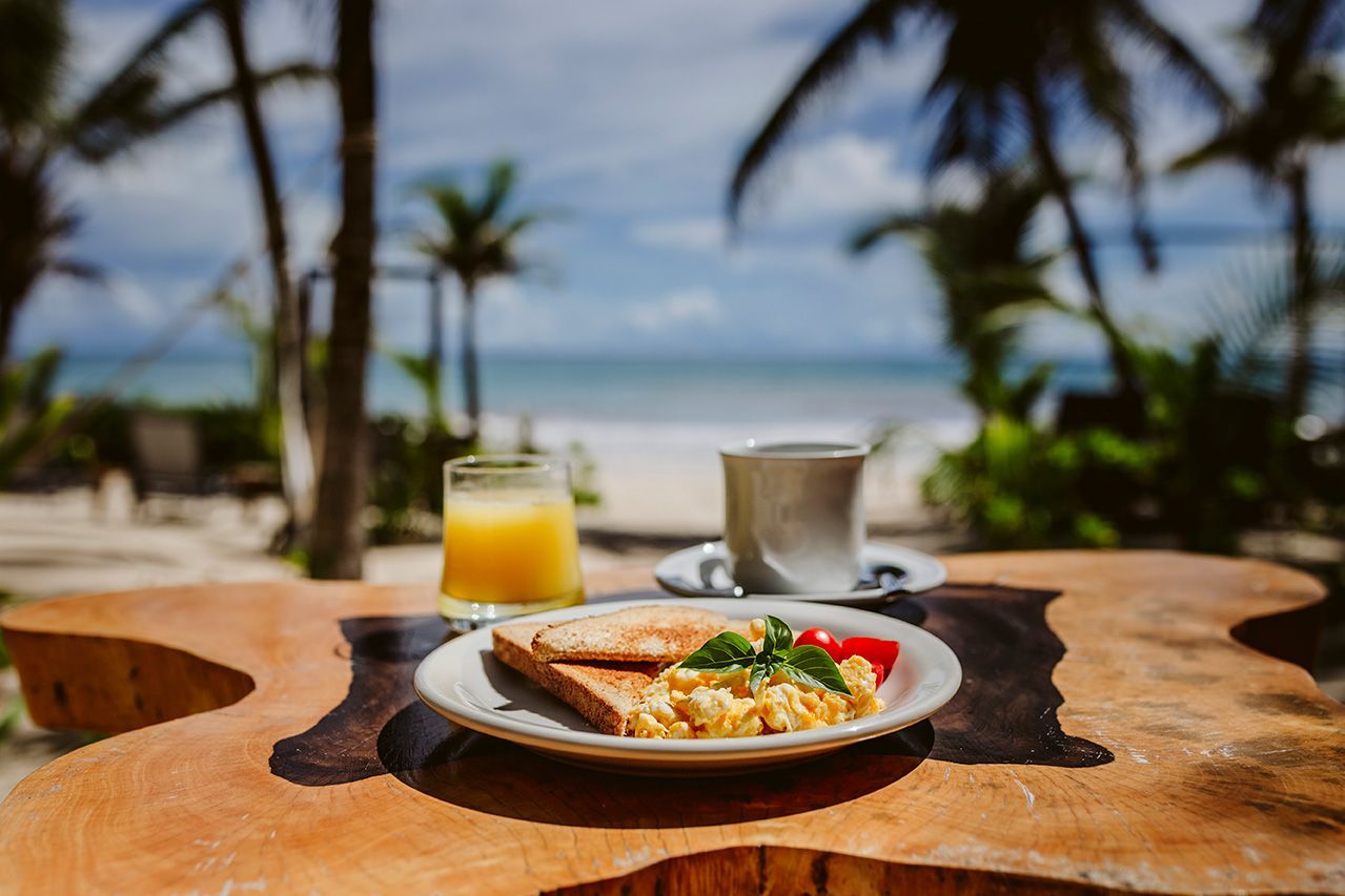 Breakfast plate, juice, and coffee on a wooden table with a beach view.