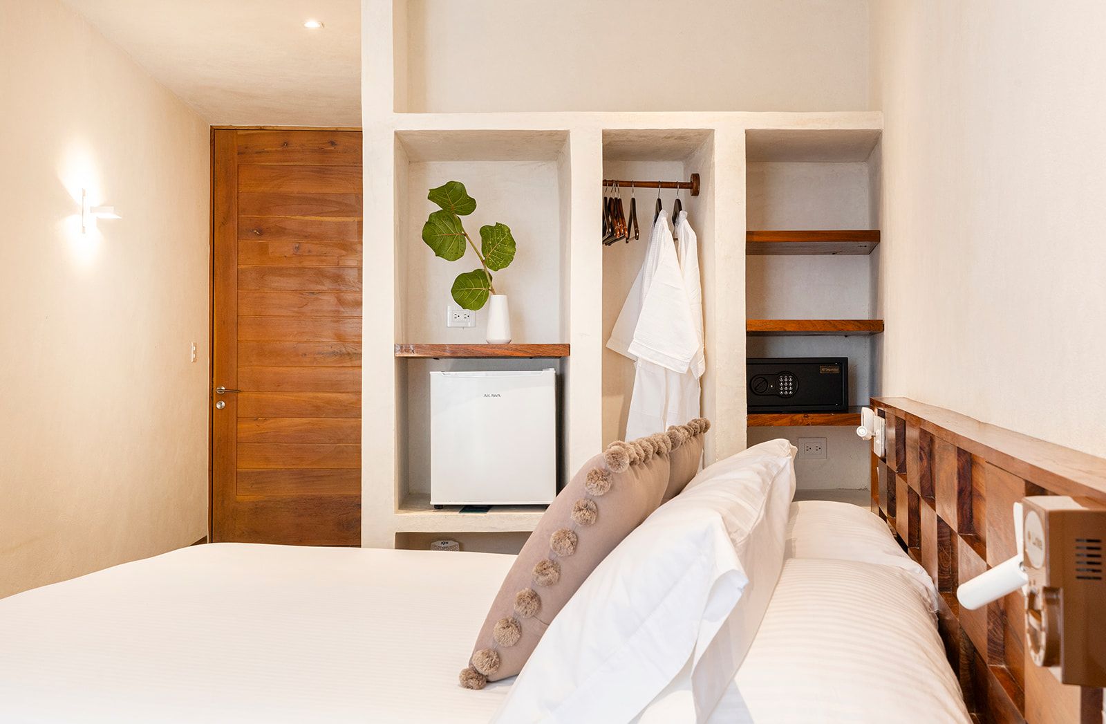 Bedroom with a bed, wooden door, built-in shelving, mini-fridge, safe, and robes hanging.