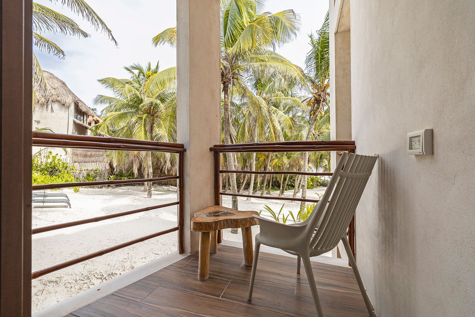 Balcony with a chair and small table overlooking a sandy area and palm trees.