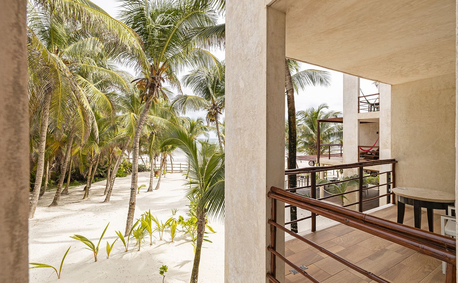 Balcony view of beach and palm trees. Sandy ground, brown railings, beige building.