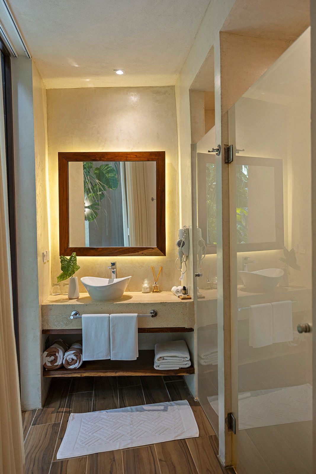 Bathroom with sink, mirror, and towels; neutral colors, wooden shelf, and white door.