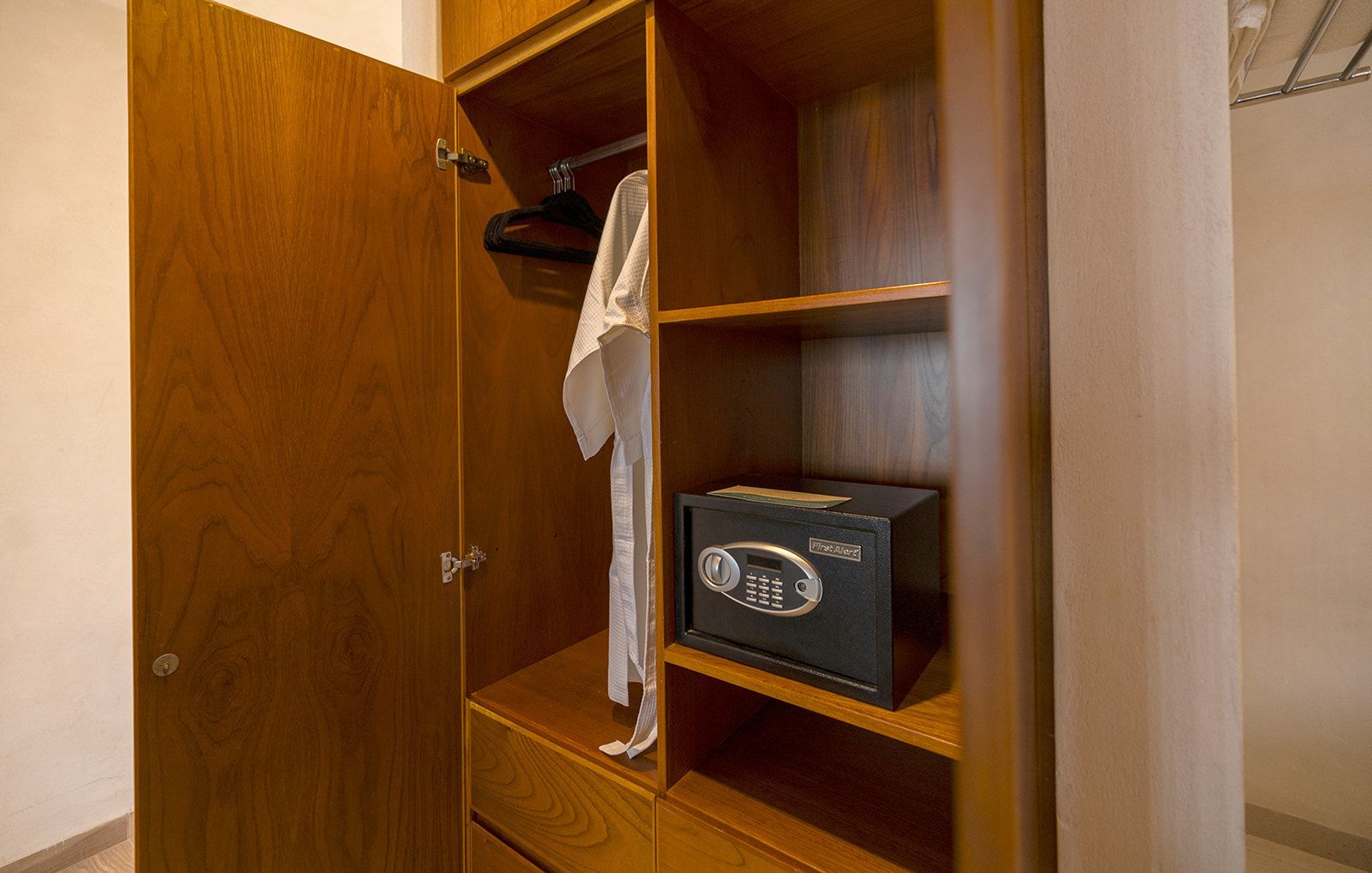 Open wooden closet with bathrobe hanging and a black safe on a shelf.