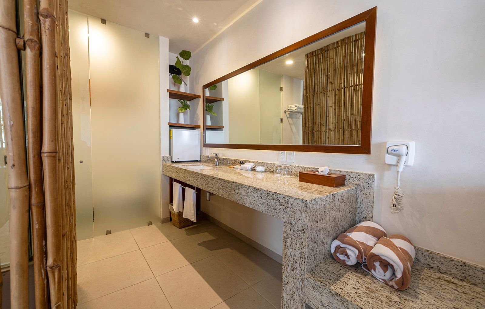 Bathroom with granite countertop, large mirror, bamboo accents, towels, and mini-fridge.