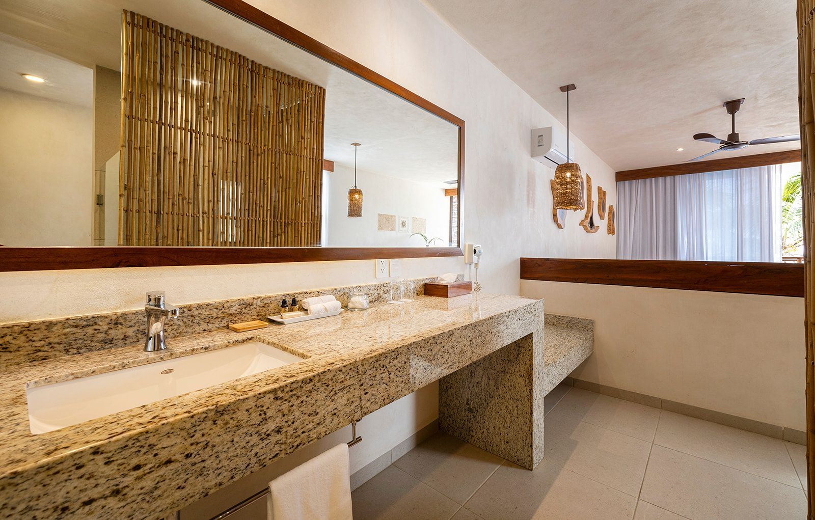 Bathroom with a marble vanity, large mirror, and bamboo wall detail; bright, airy space.