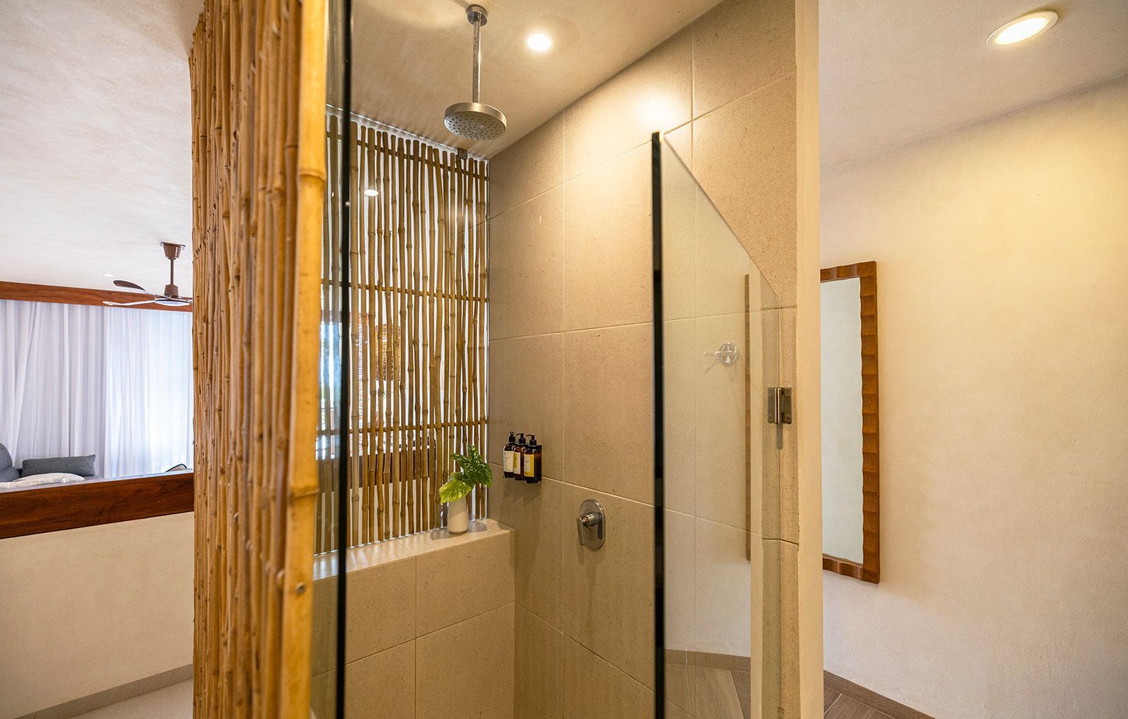 Shower area with bamboo, glass, and neutral-colored tile. A mirror is on the right.