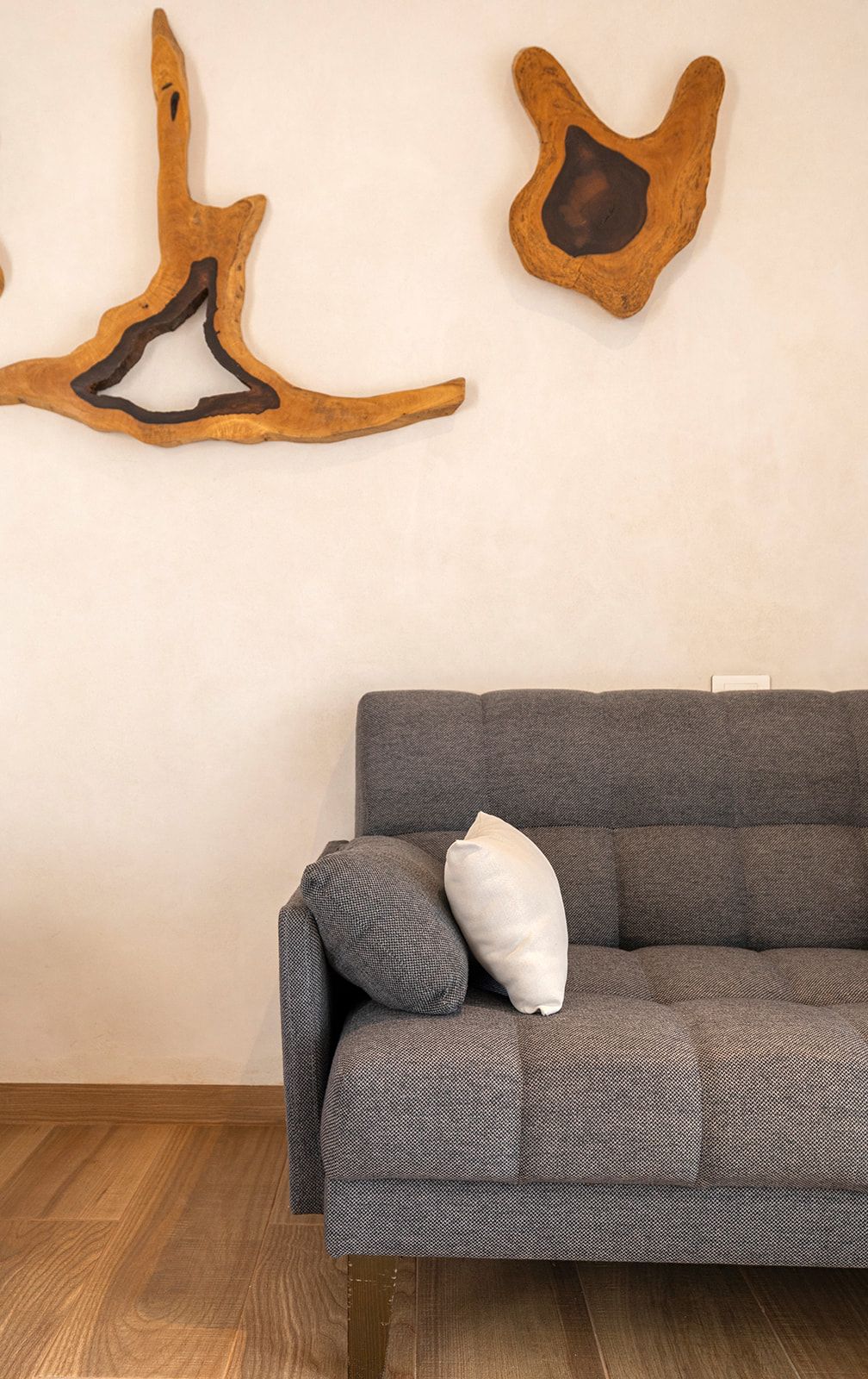 Gray sofa against a beige wall with wood art pieces. Wooden floor.