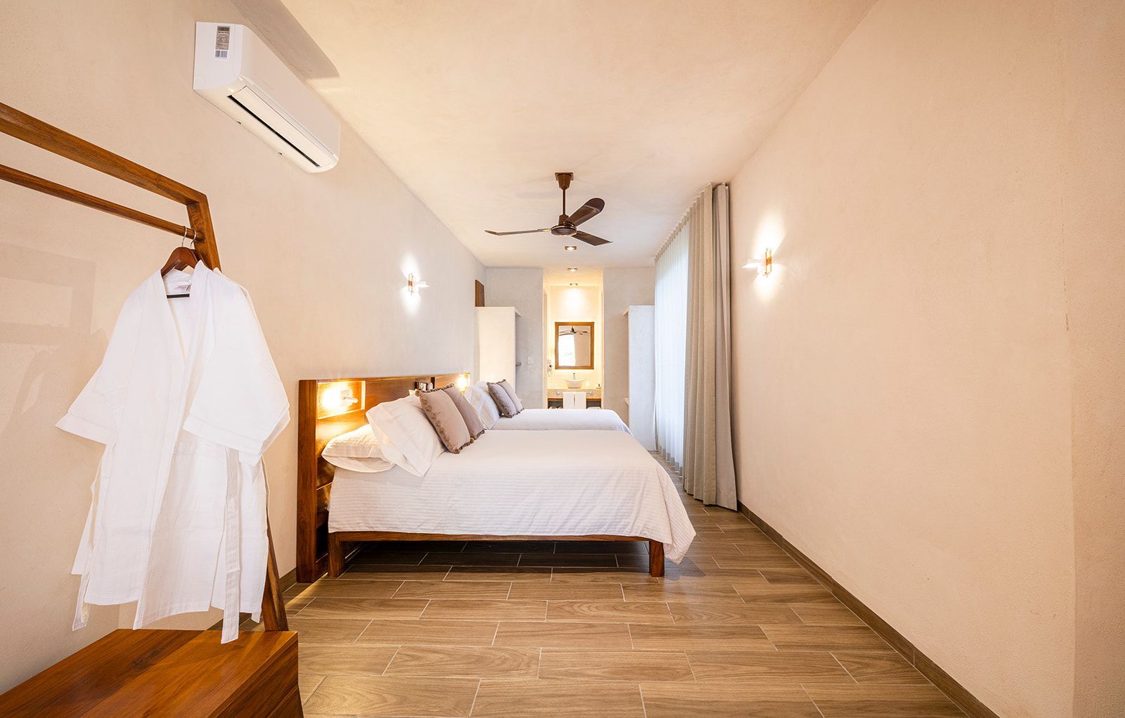 Bedroom with two beds, wooden headboard, robe hanging on a rack, and a ceiling fan.