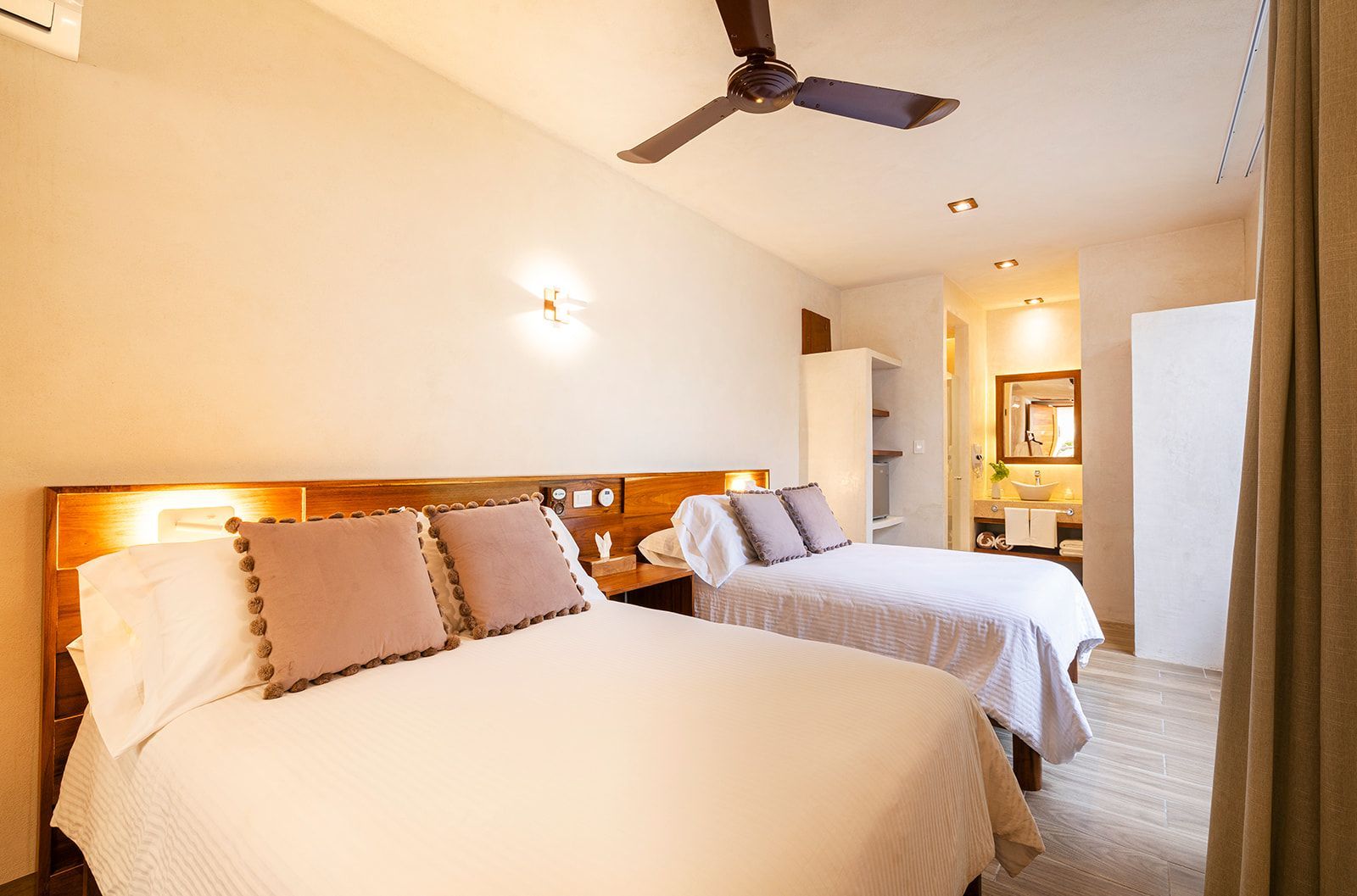 Hotel room with two queen beds, nightstand, ceiling fan, and glimpse of a bathroom.