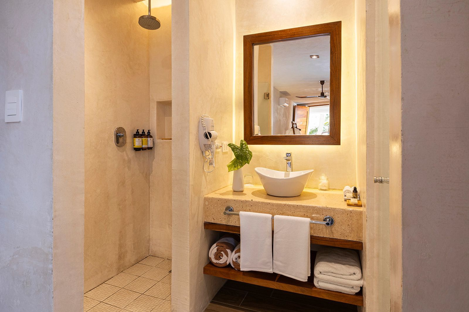 Bathroom with shower, sink, and mirror. Beige walls, stone countertop, wooden accents.