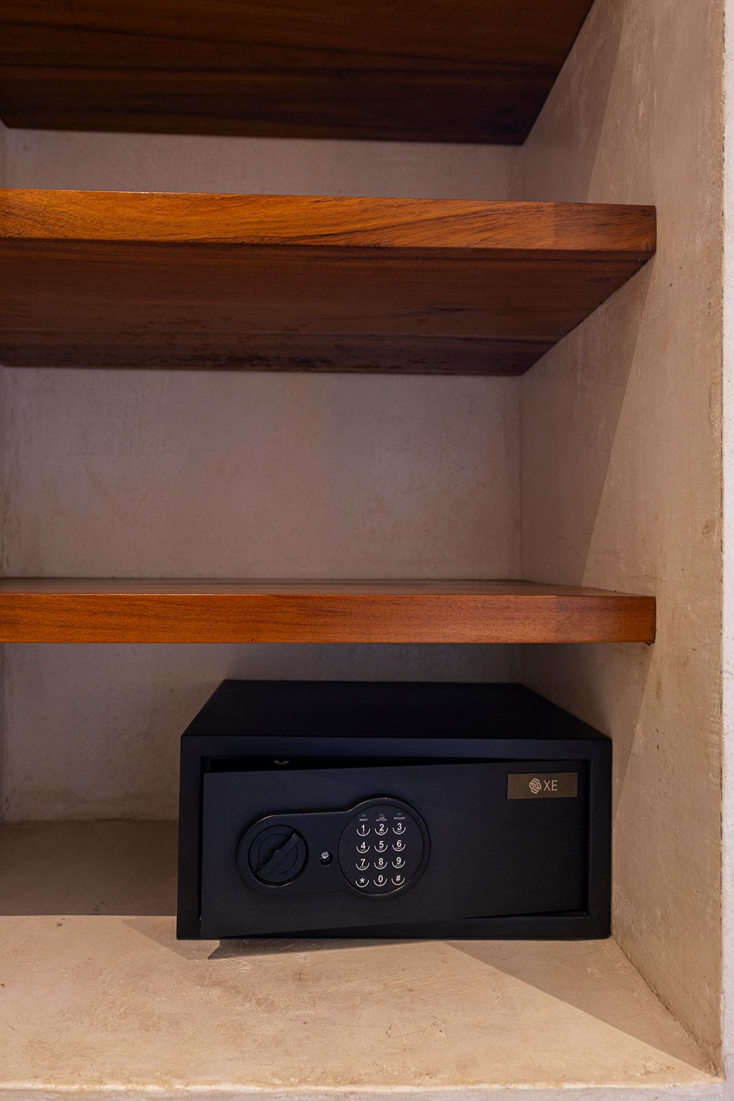 Black safe on a shelf inside a recessed alcove with wooden shelves.