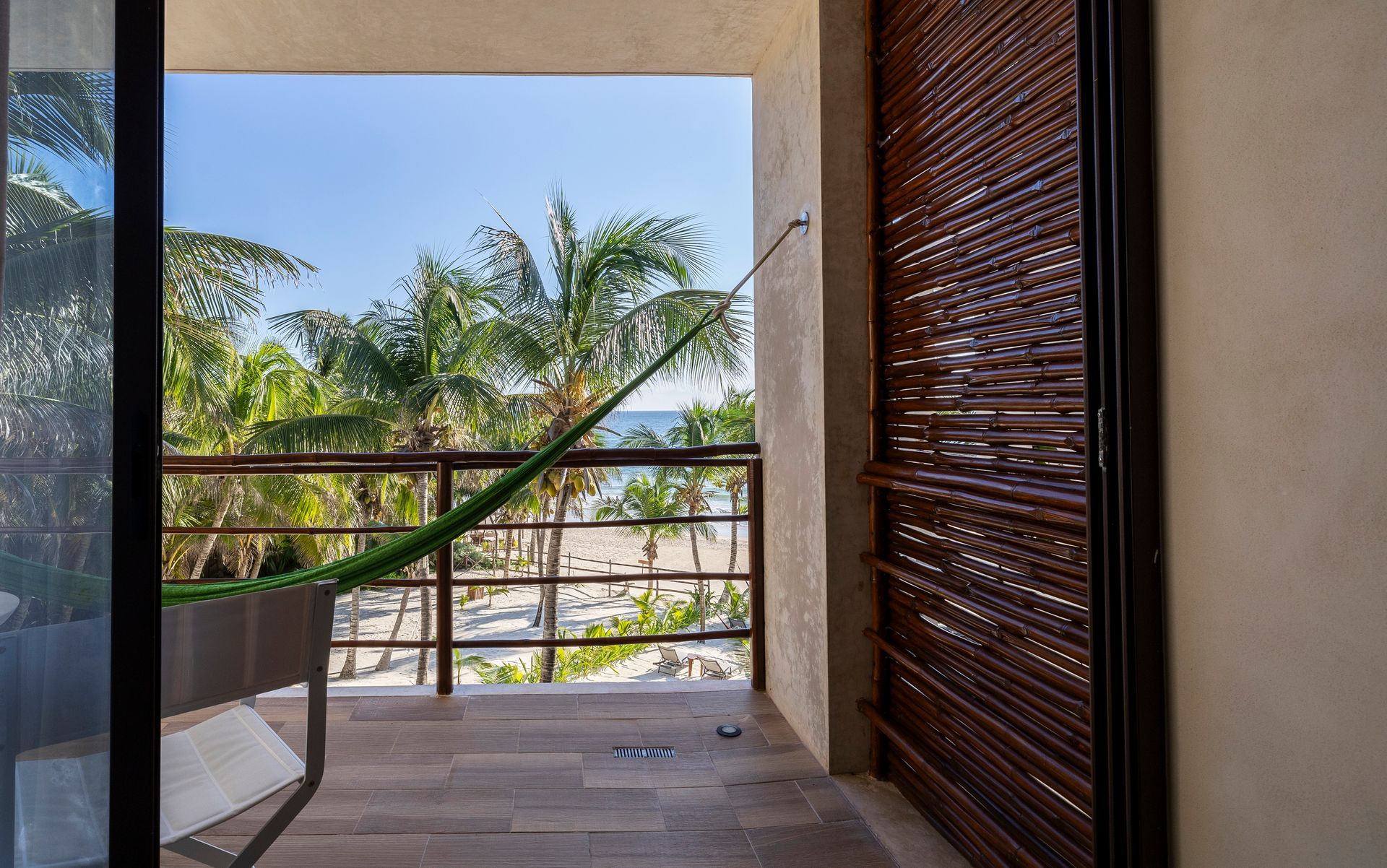 View from a room's balcony with a hammock, looking out at a beach, palm trees, and ocean.
