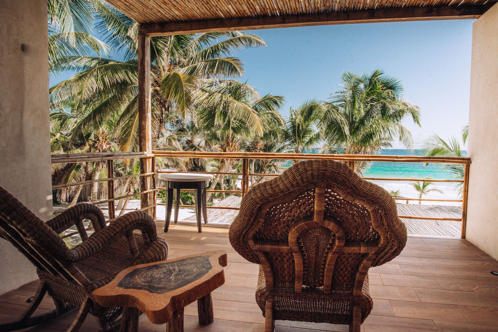 Balcony overlooking a beach, with wicker furniture, palm trees, and ocean view.