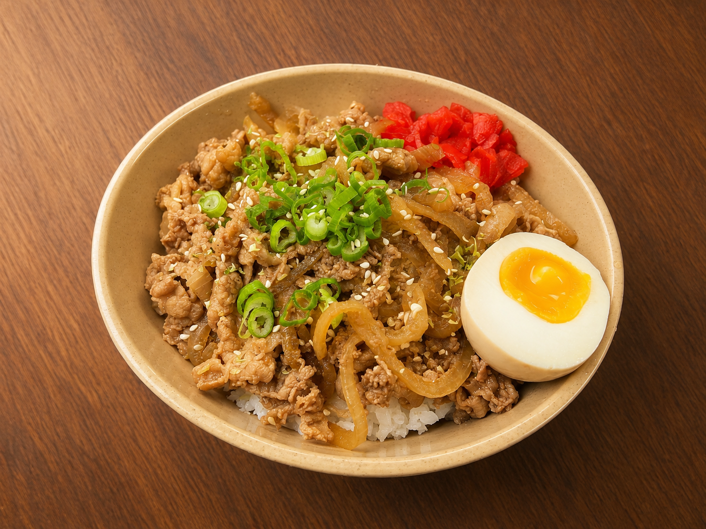 Beef rice bowl topped with green onions, pickled ginger, and a halved soft-boiled egg on a wooden table