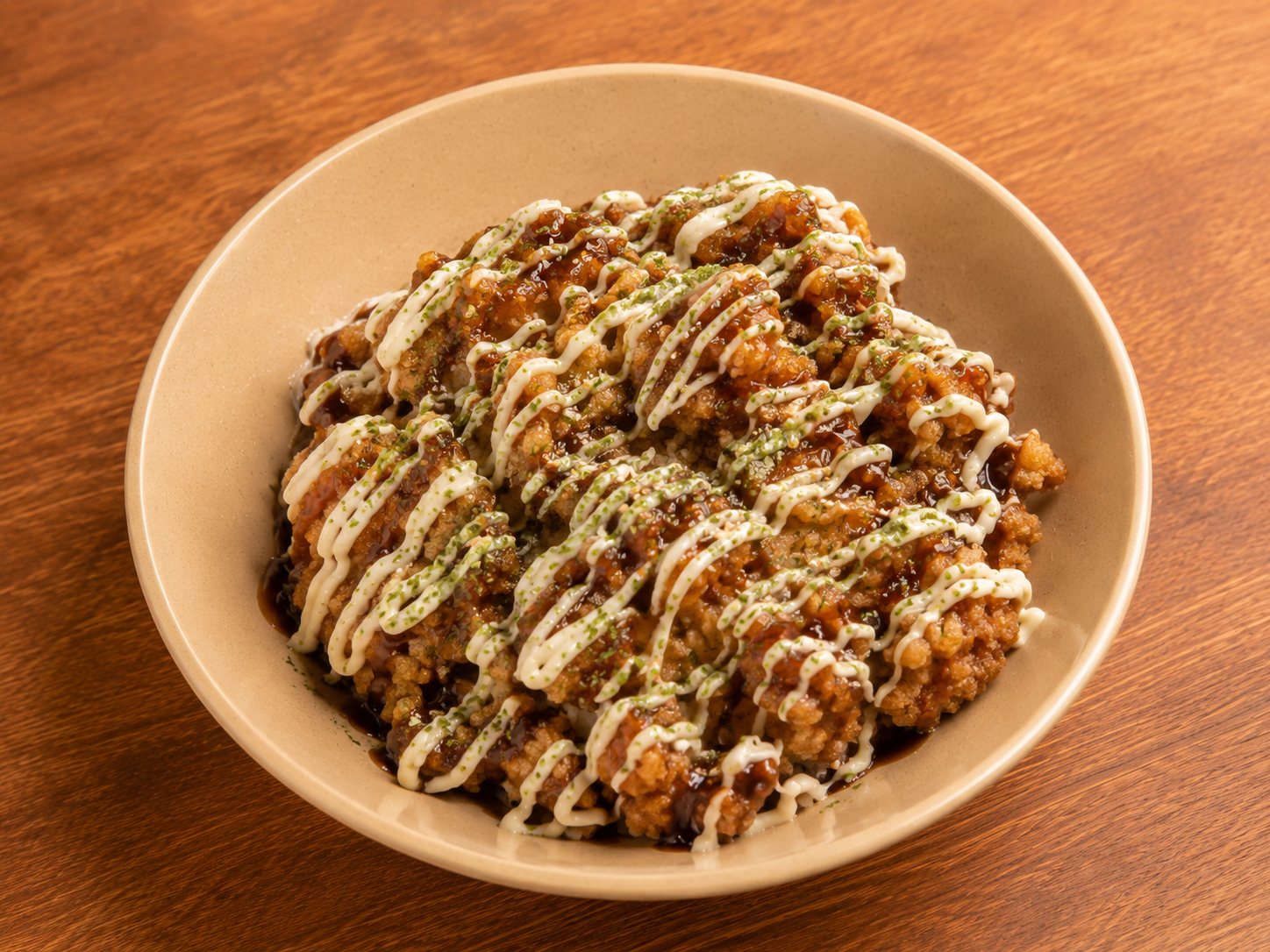 Bowl of fried chicken bites drizzled with white sauce on a wooden table