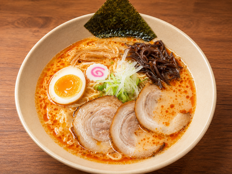 Bowl of ramen with sliced pork, soft-boiled egg, seaweed, narutomaki, and scallions in red broth