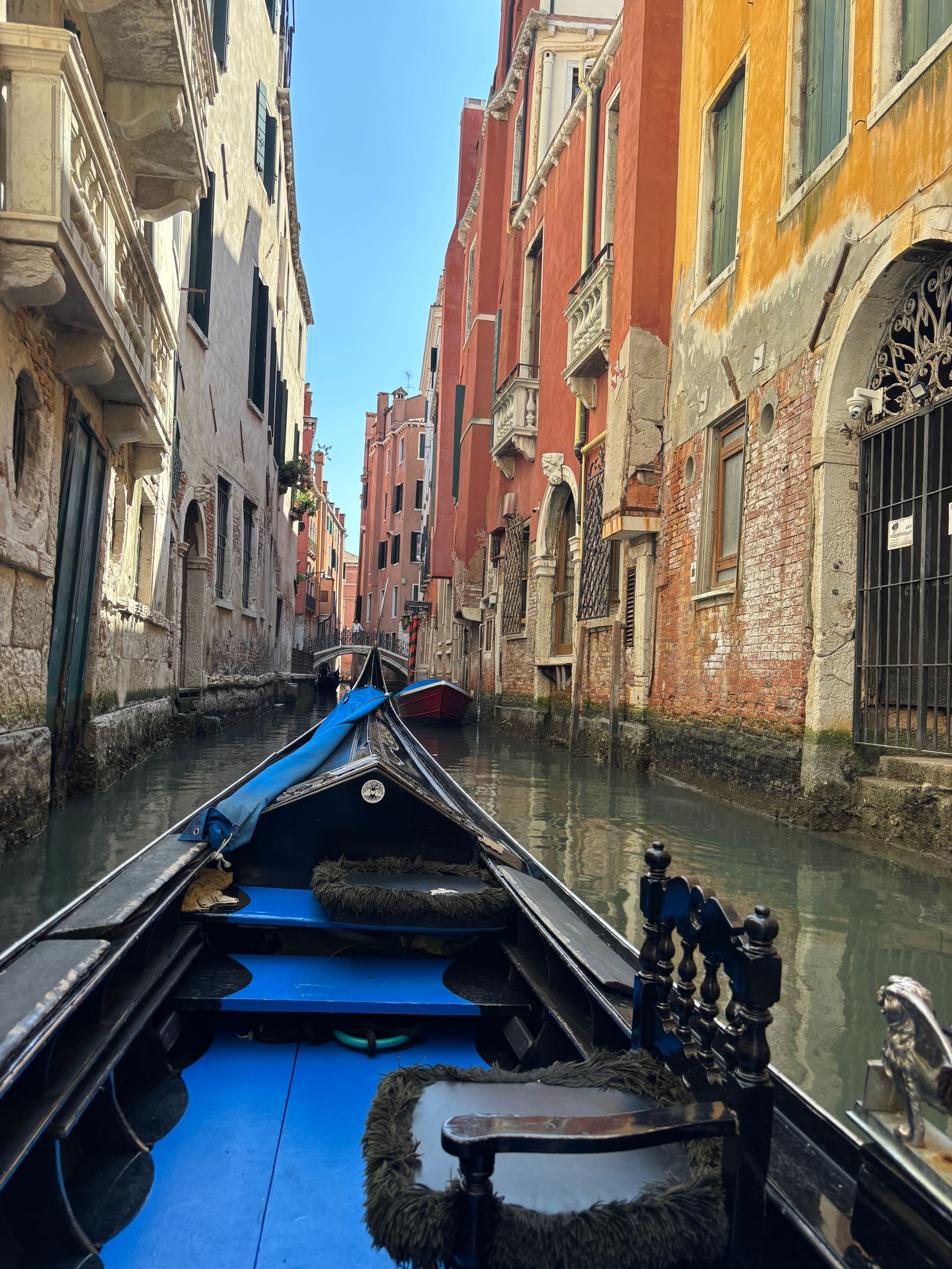 Gondola travels through narrow Venetian canal; aged buildings line the water. Blue gondola interior visible.