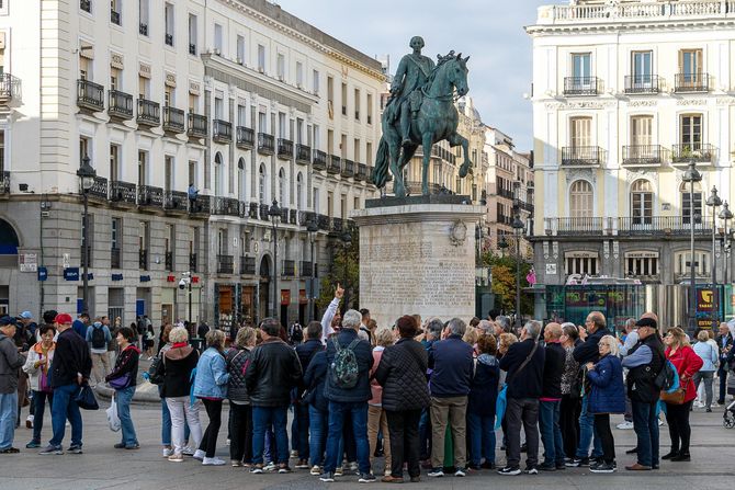 Statue of a man on horseback in Madrid square, surrounded by a crowd of tourists and buildings.