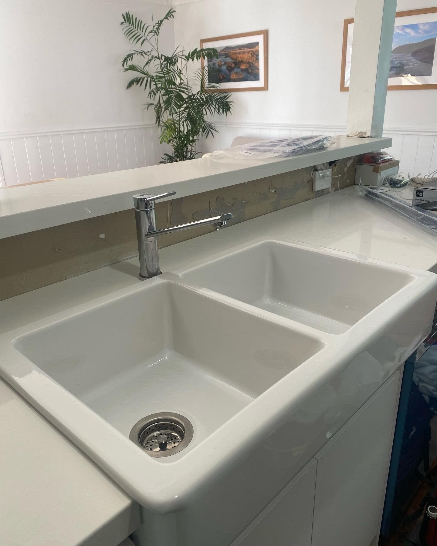 A white, double-basin farmhouse kitchen sink with a chrome faucet, set into a countertop in a kitchen. — Distinct Plumbing Services In Kiama, NSW
