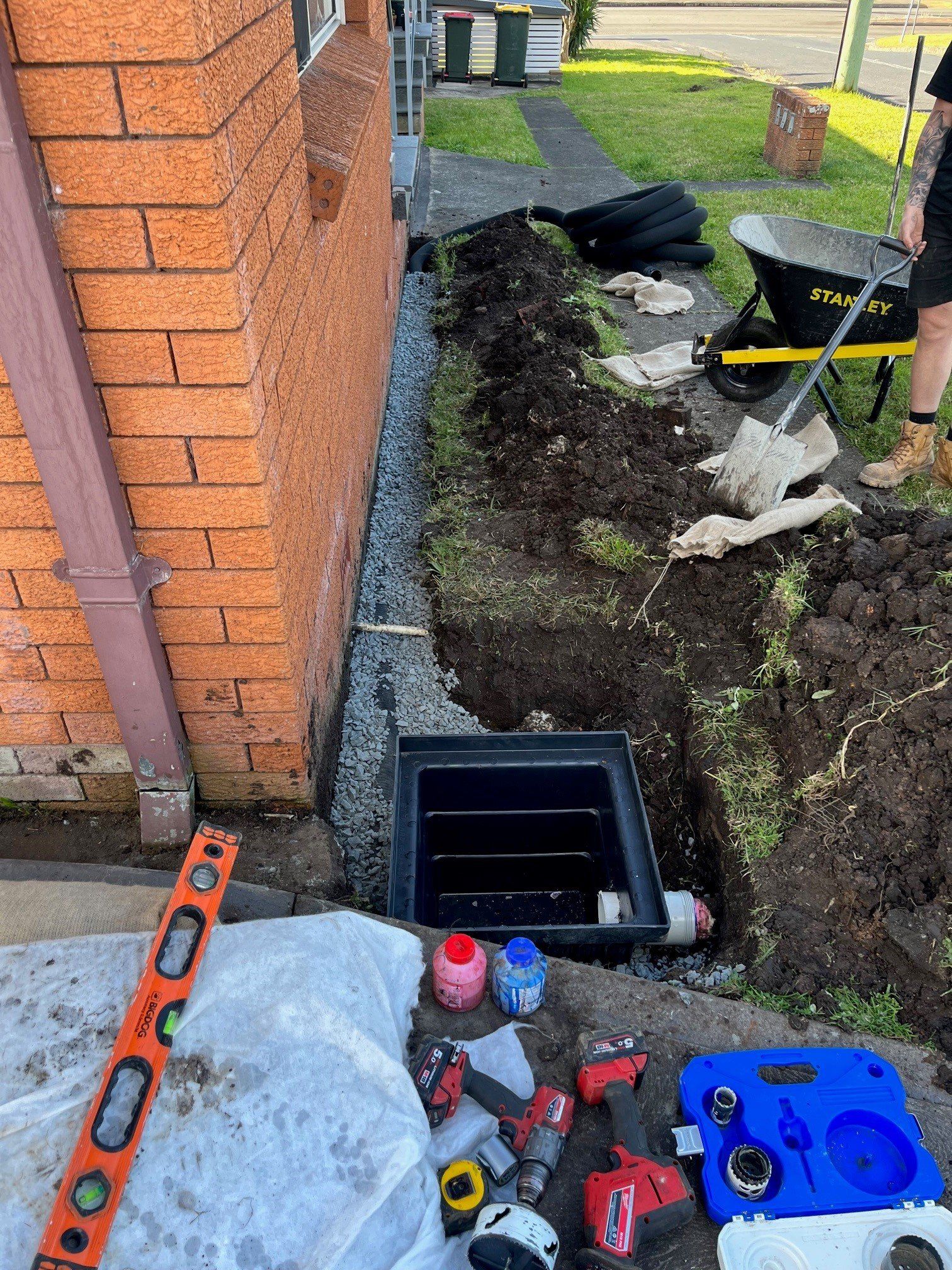 A black box in a hole dug in the ground with tools— Distinct Plumbing Services In Kiama, NSW