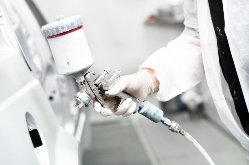 A Person in a White Coat Holds a Spray Gun — Camden Haven Panel Works In Laurieton, NSW