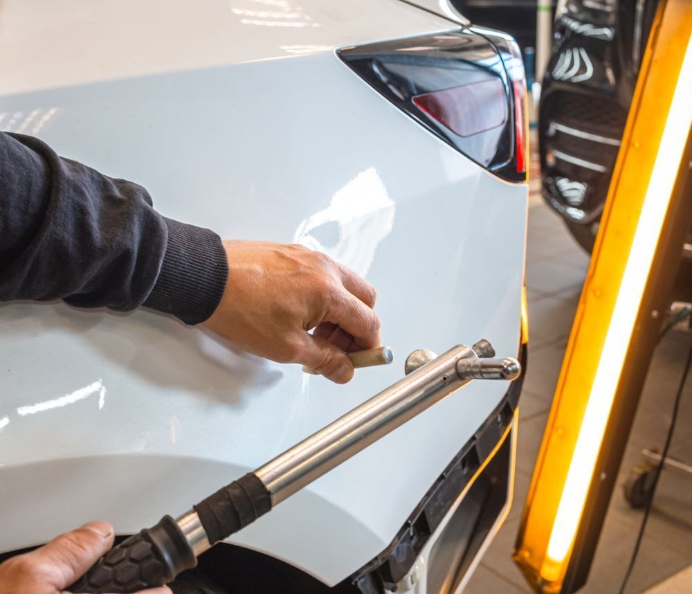 A Man is Working on a White Car With a Tool — Camden Haven Panel Works In Laurieton, NSW