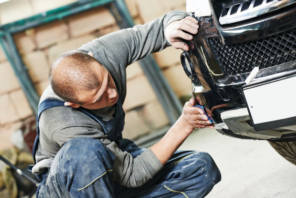 A Man is Working on the Front of a Car in a Garage — Camden Haven Panel Works In Laurieton, NSW