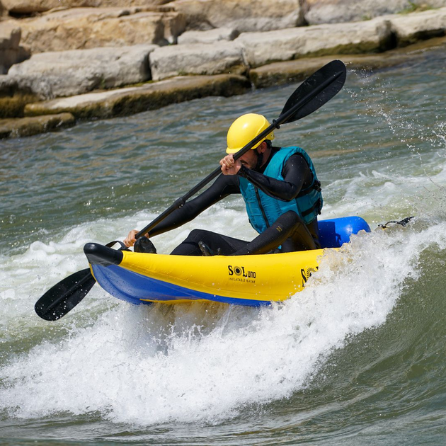 Kayaker in yellow helmet paddling a blue-and-yellow kayak through whitewater