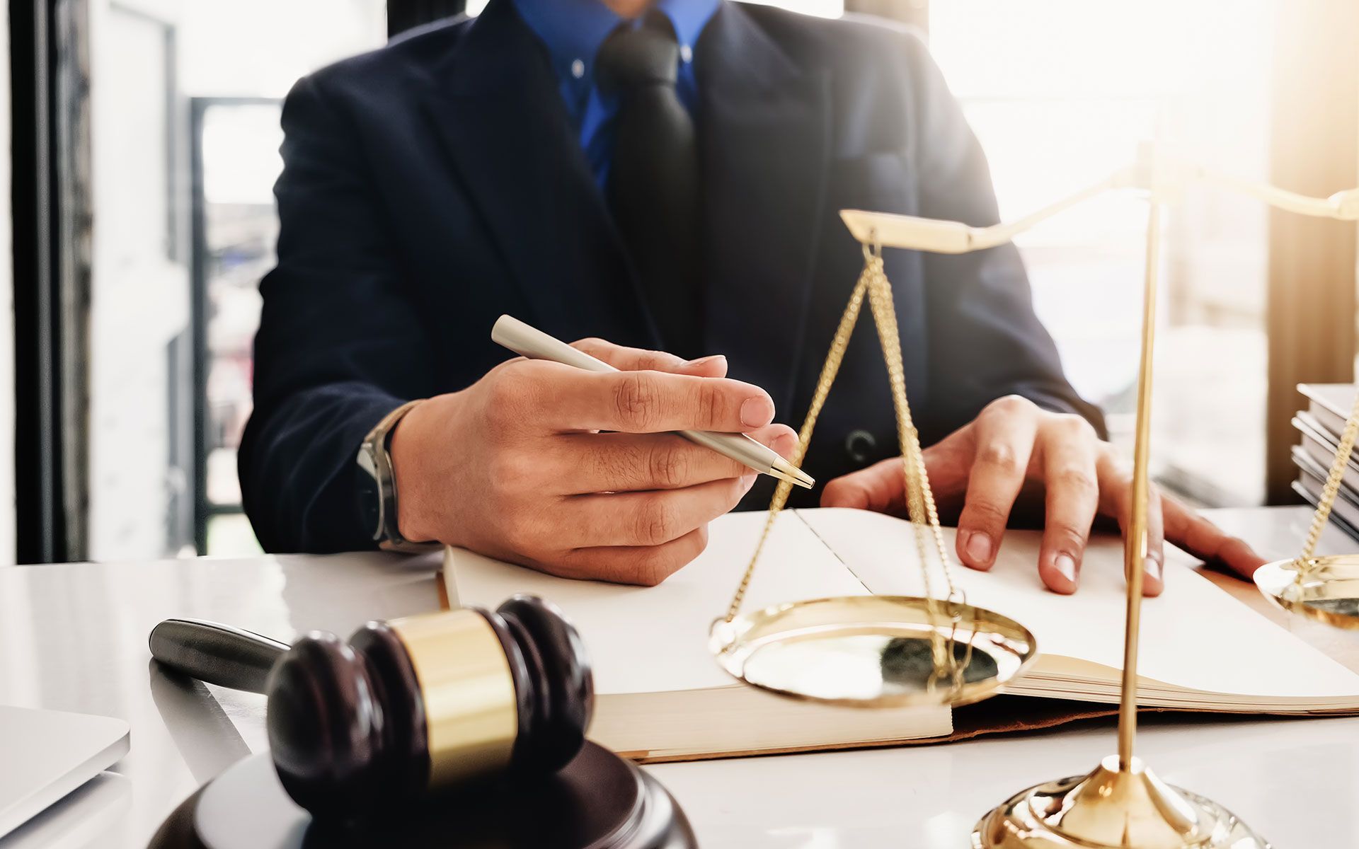 A person in a suit at a desk with a gavel, scales of justice, and a notebook.