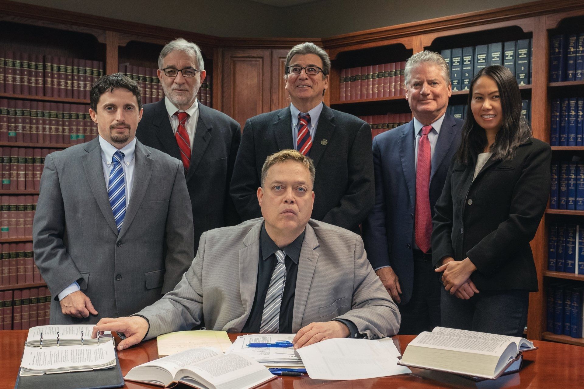 Group of six lawyers posing in front of bookshelves. One is seated, the others standing. Dark suits, ties.