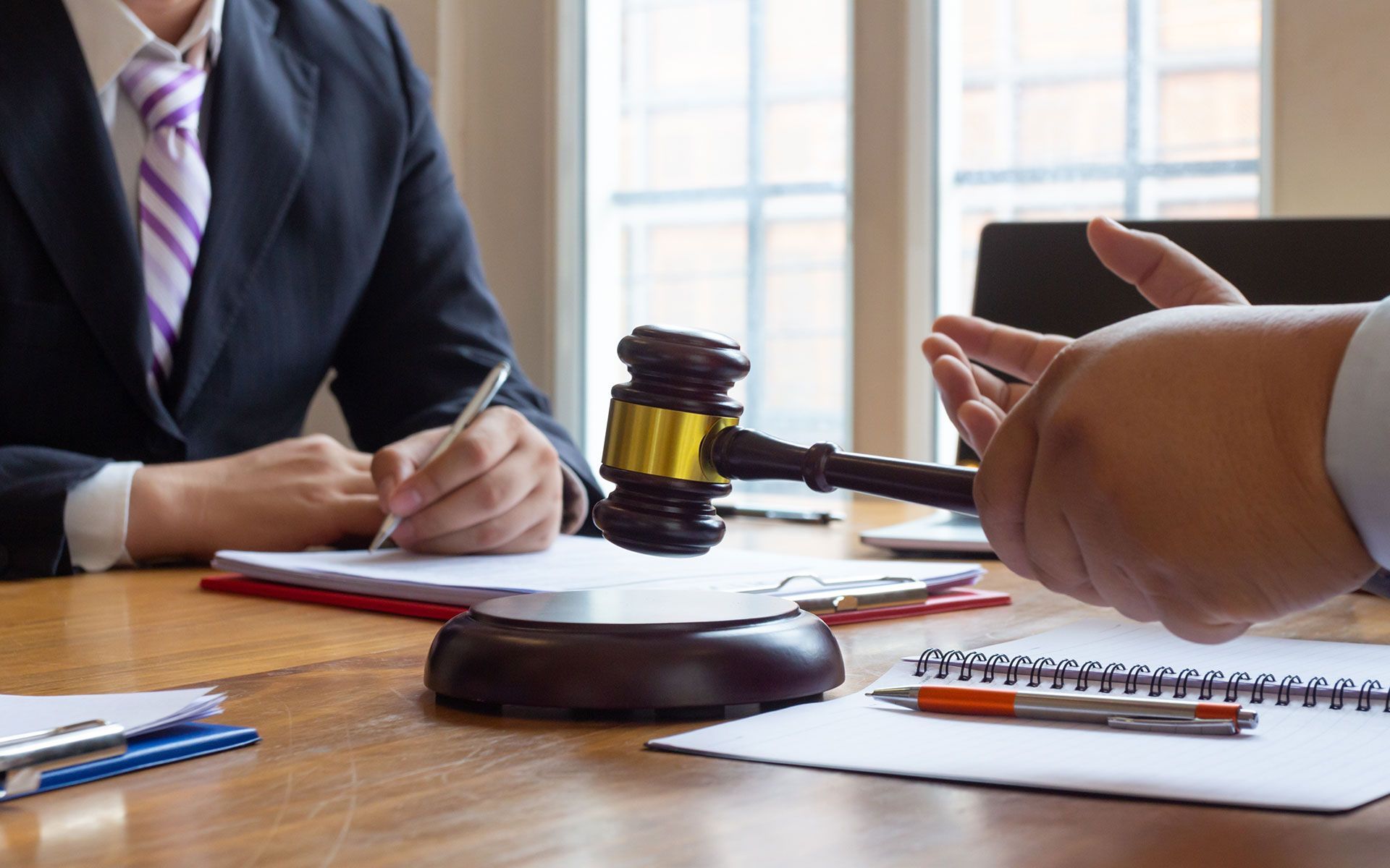 Two lawyers in a law office, one writing, the other gesturing with a gavel and hand.