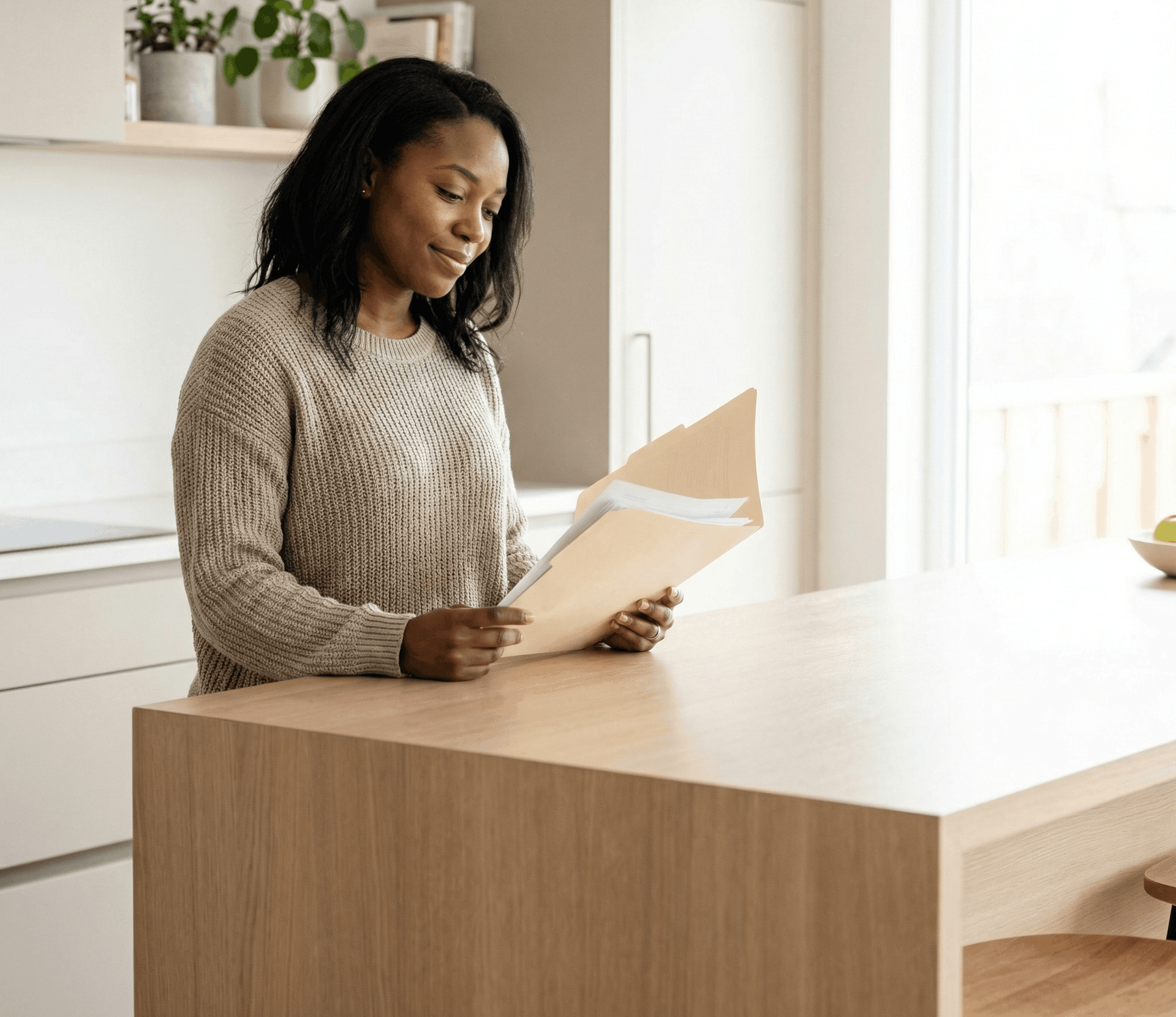 Woman in sweater reads documents at a kitchen island in a modern kitchen.