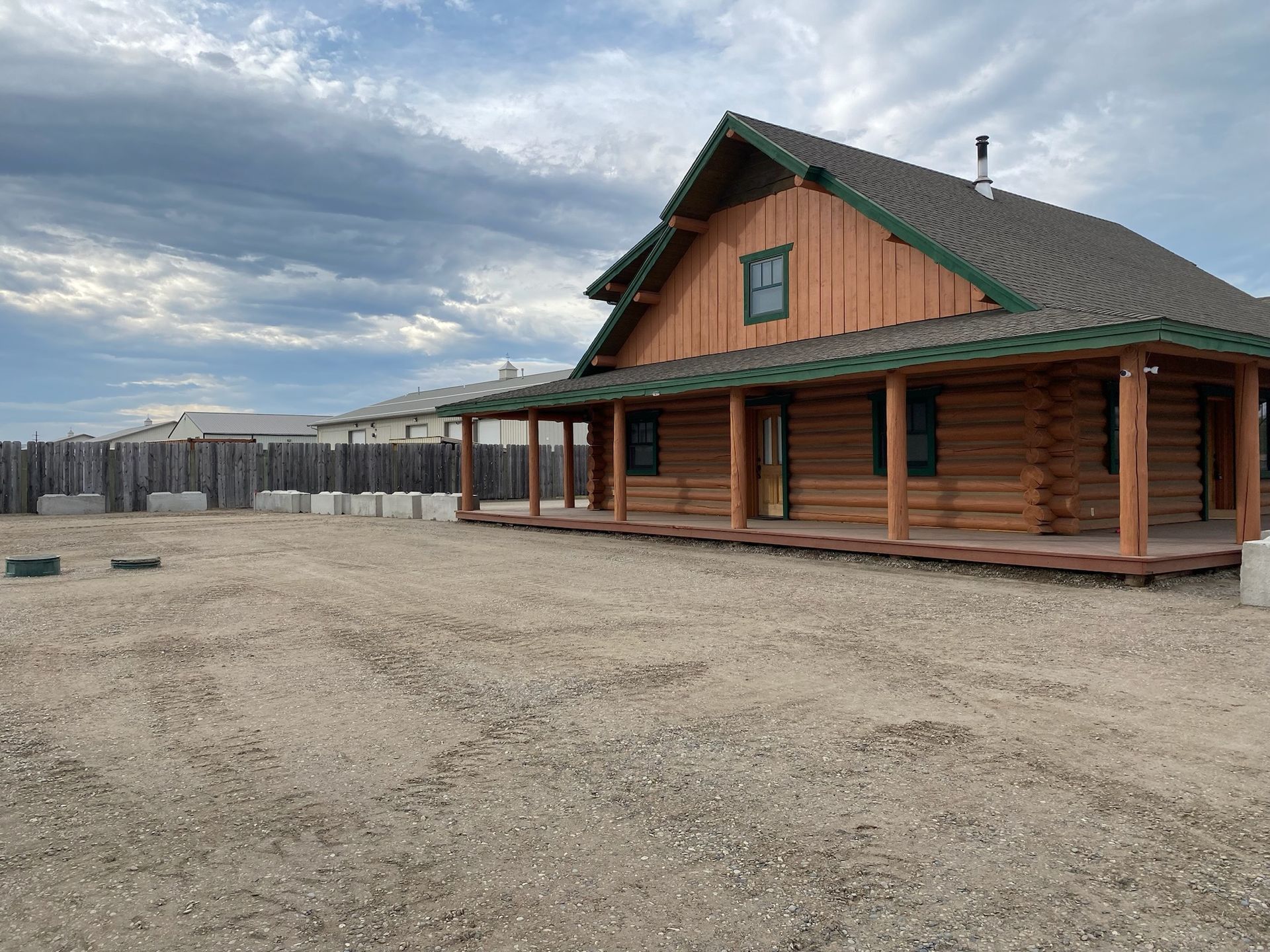 A log cabin with a porch is sitting in the middle of a dirt field.
