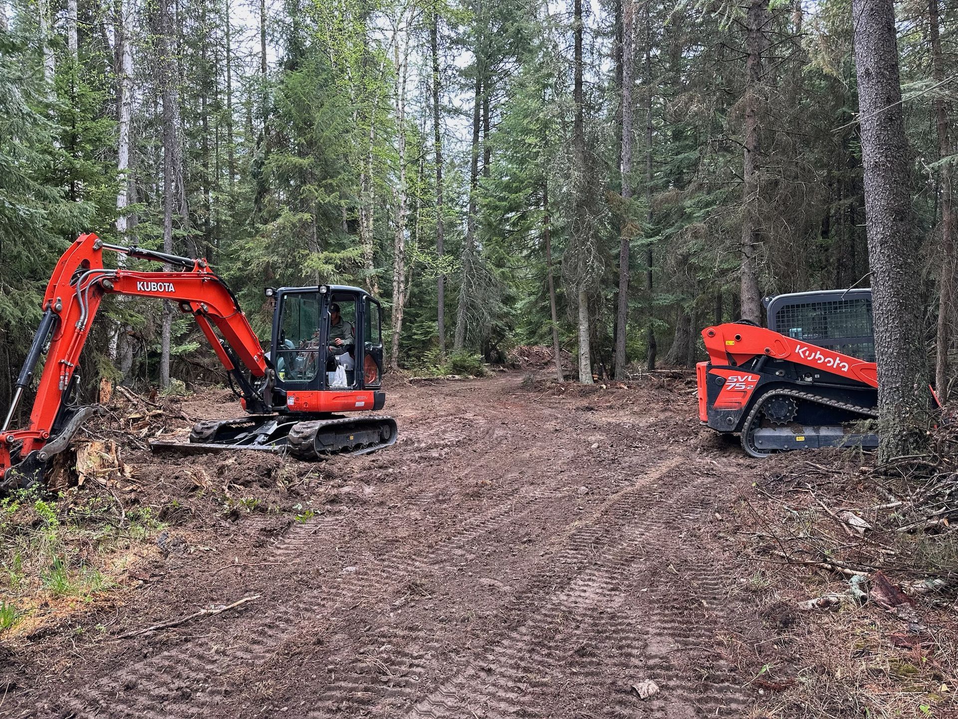 Two tractors are sitting on a dirt road in the woods.