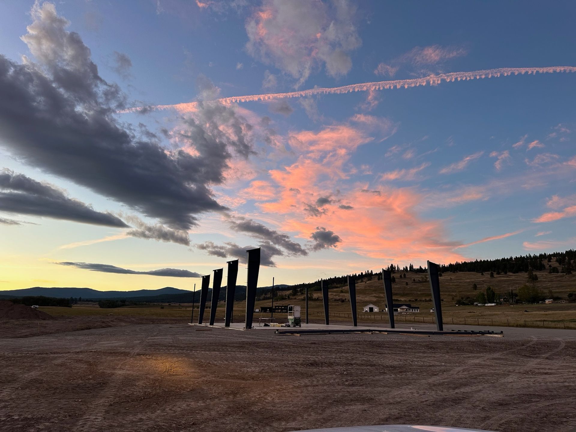 A sunset over a dirt field with a row of wooden posts in the foreground.