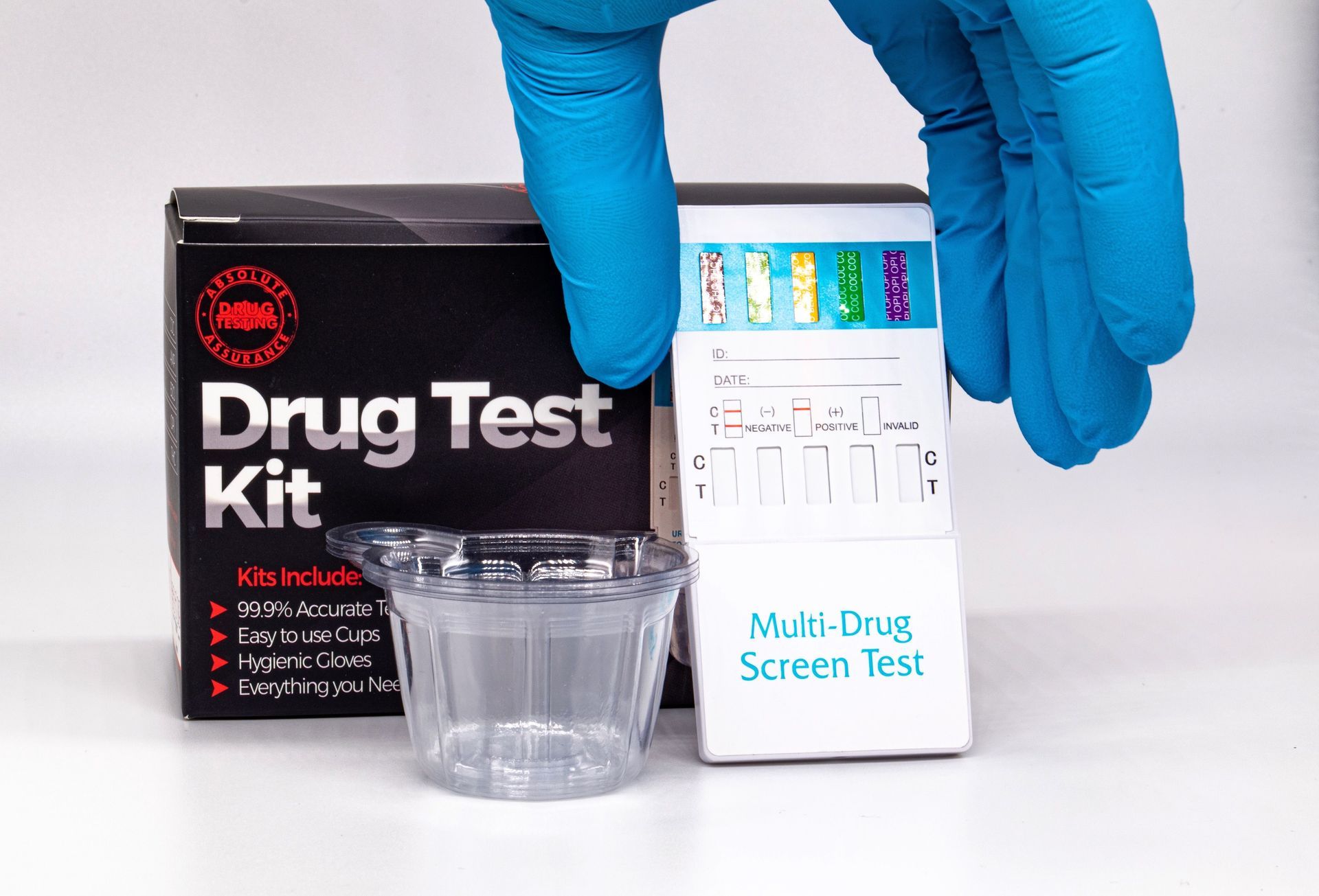 Blue-gloved hands holding a multi-drug screen test kit with a sample cup and test box