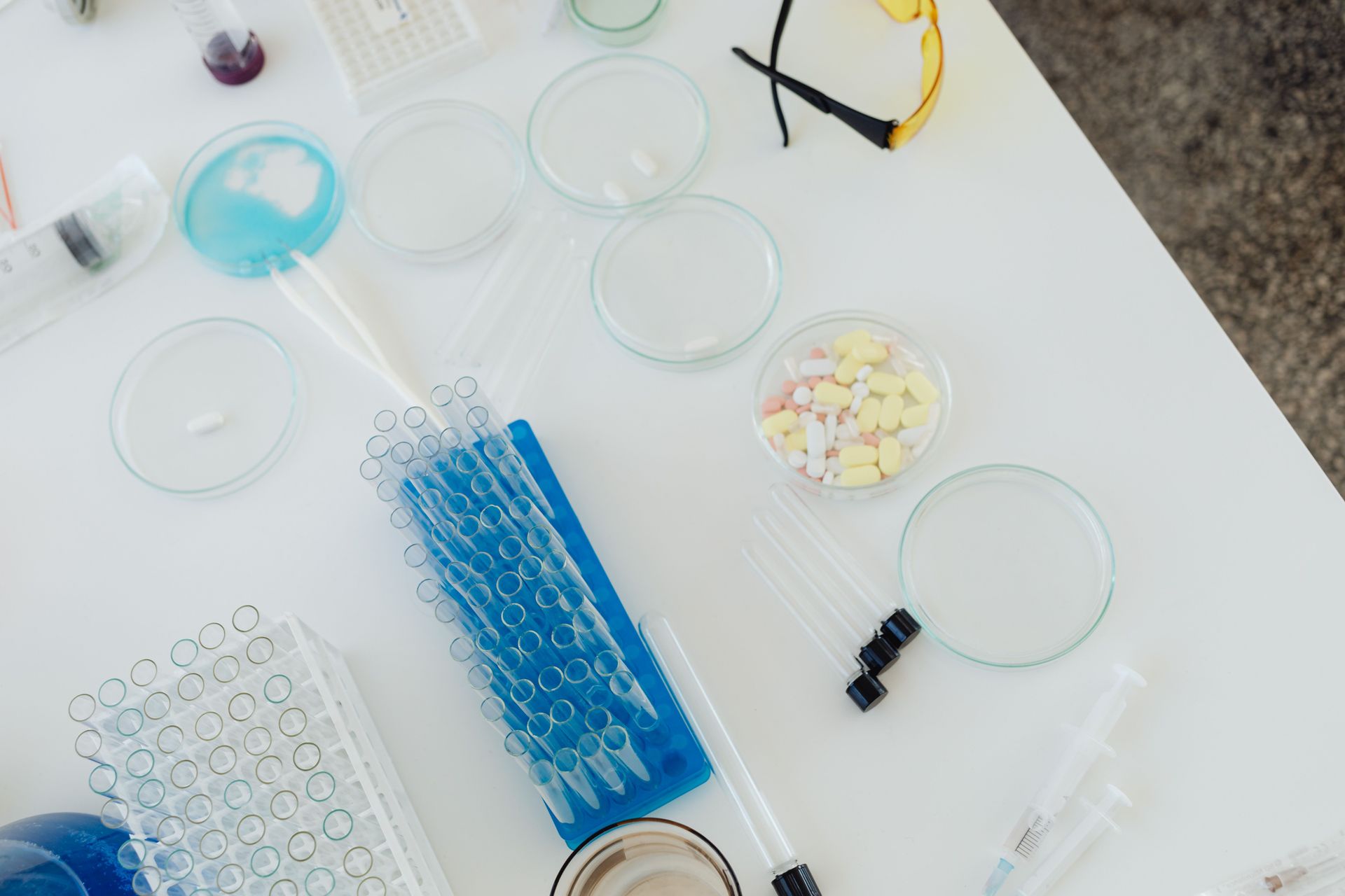 Lab bench with pipettes, petri dishes, test tubes, and small lab tools on a white surface