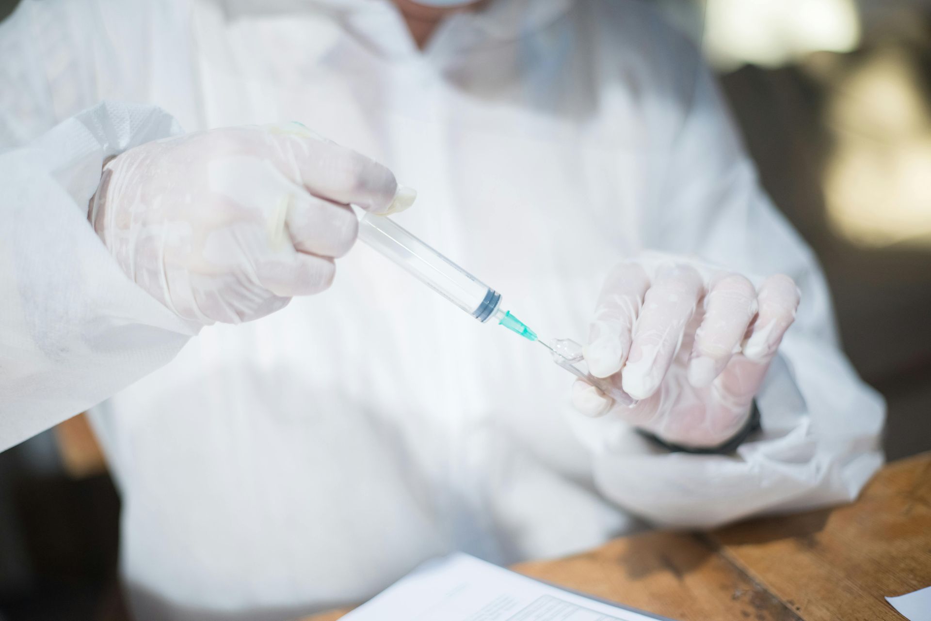 Person in protective suit and gloves preparing a syringe.